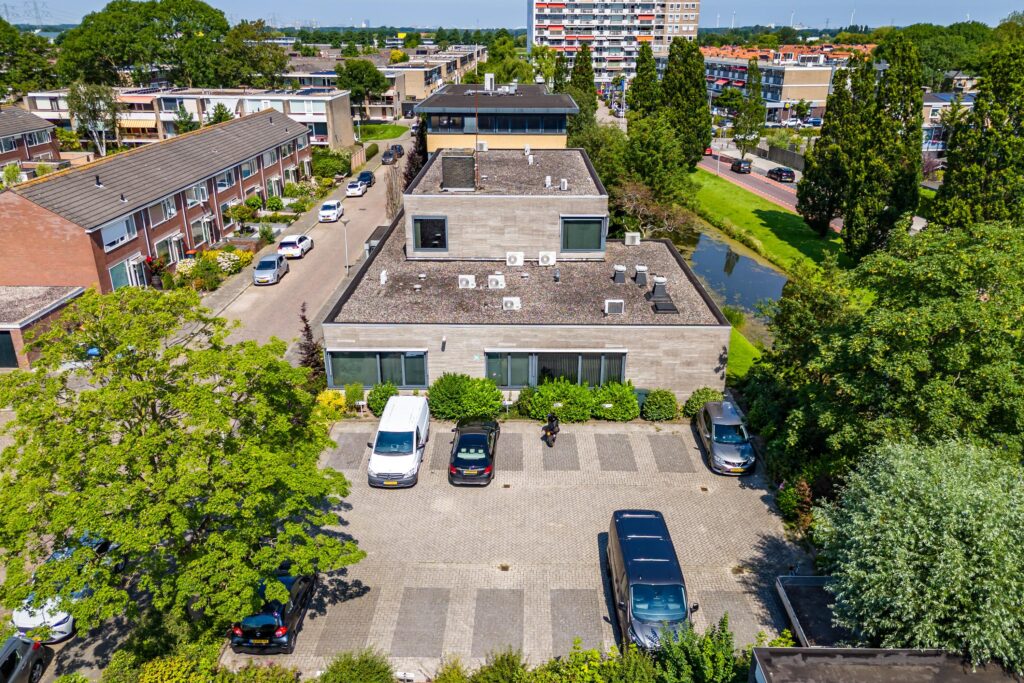 Luchtfoto van een modern gebouw en parkeerplaatsen aan de Nicolaas Pieckstraat, omringd door groen en woningen.