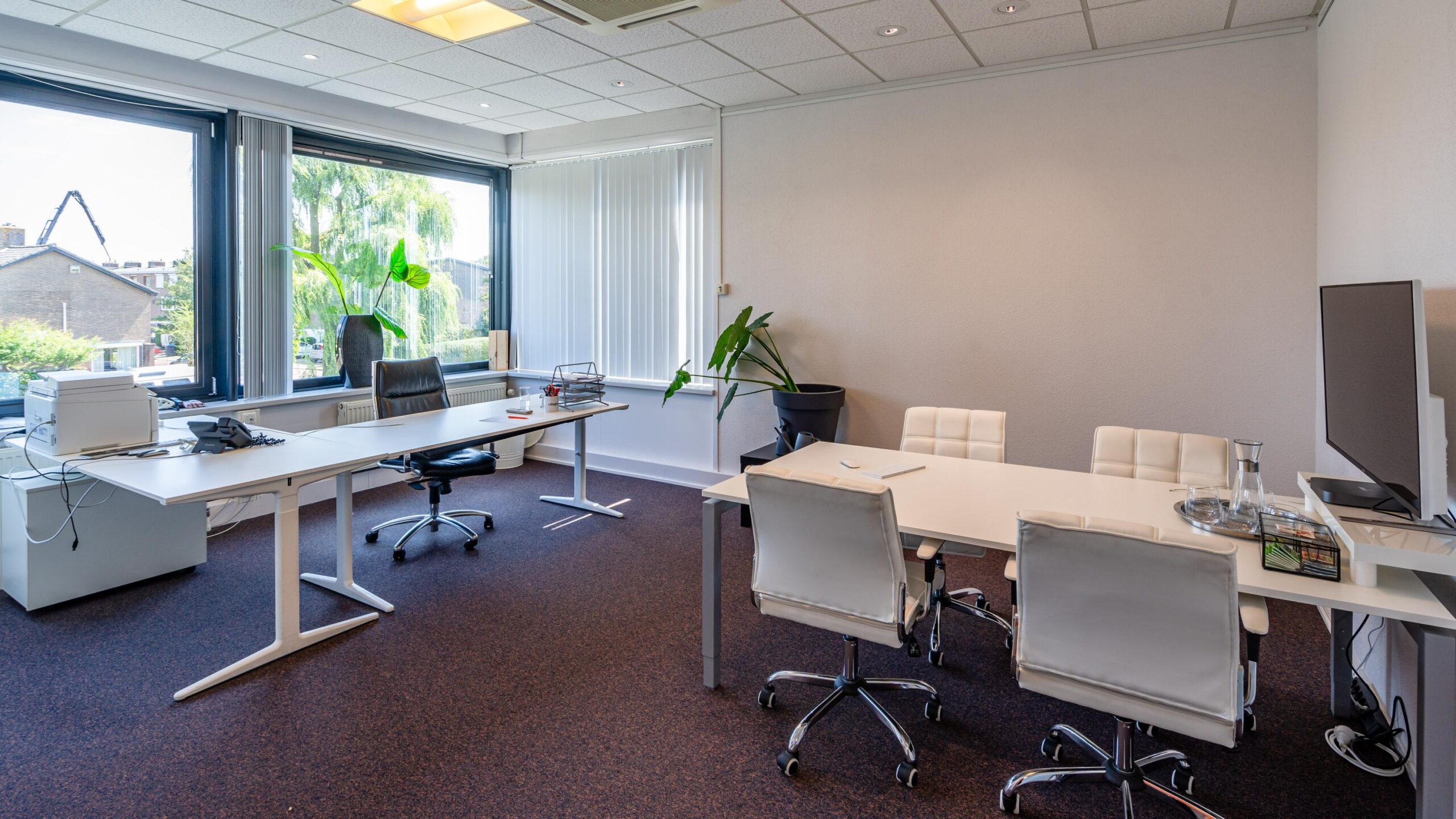 Een moderne kantoorruimte met bureaus, stoelen, planten en grote ramen.