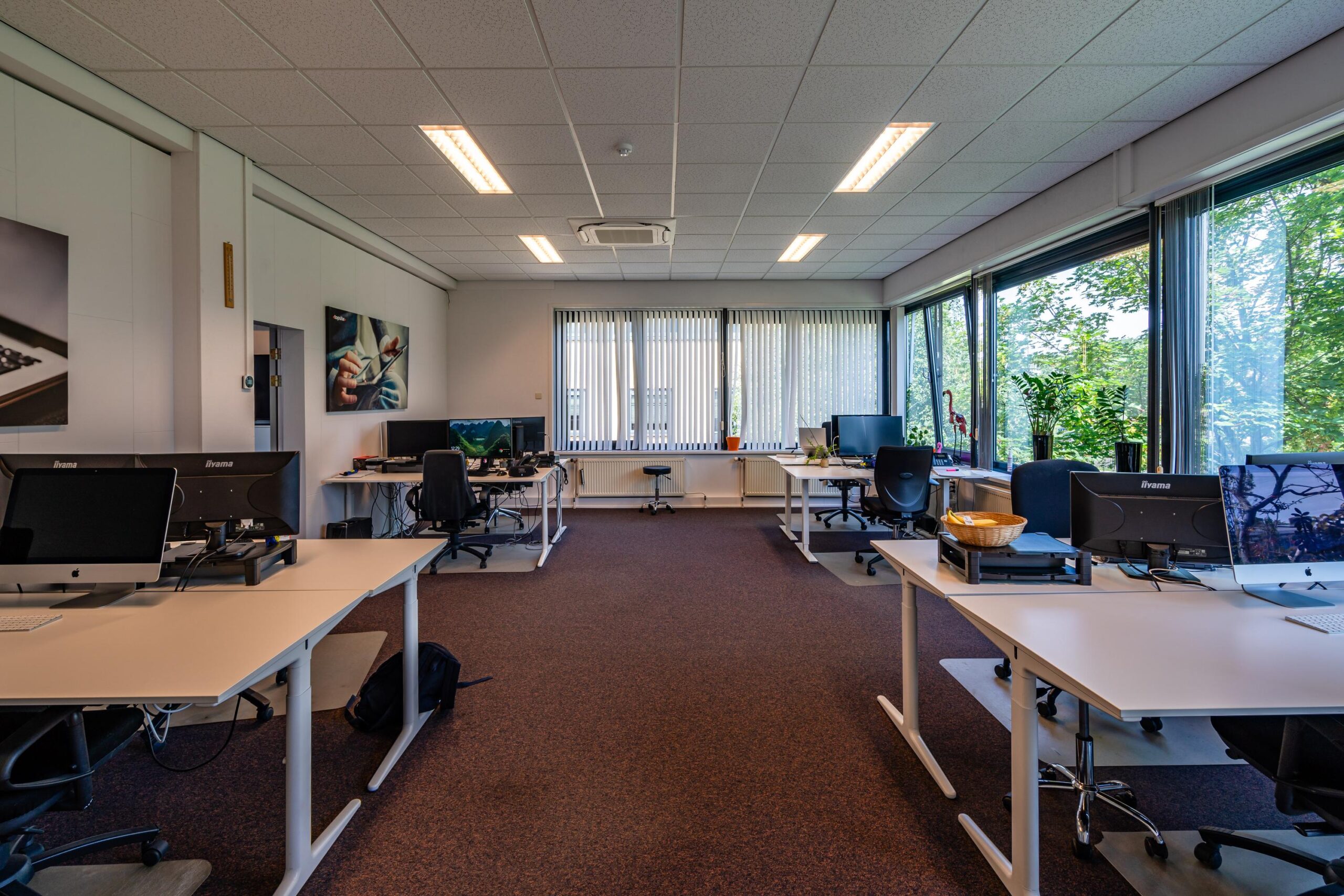 Een ruim en modern kantoor met meerdere werkplekken en grote ramen die uitkijken op groen.