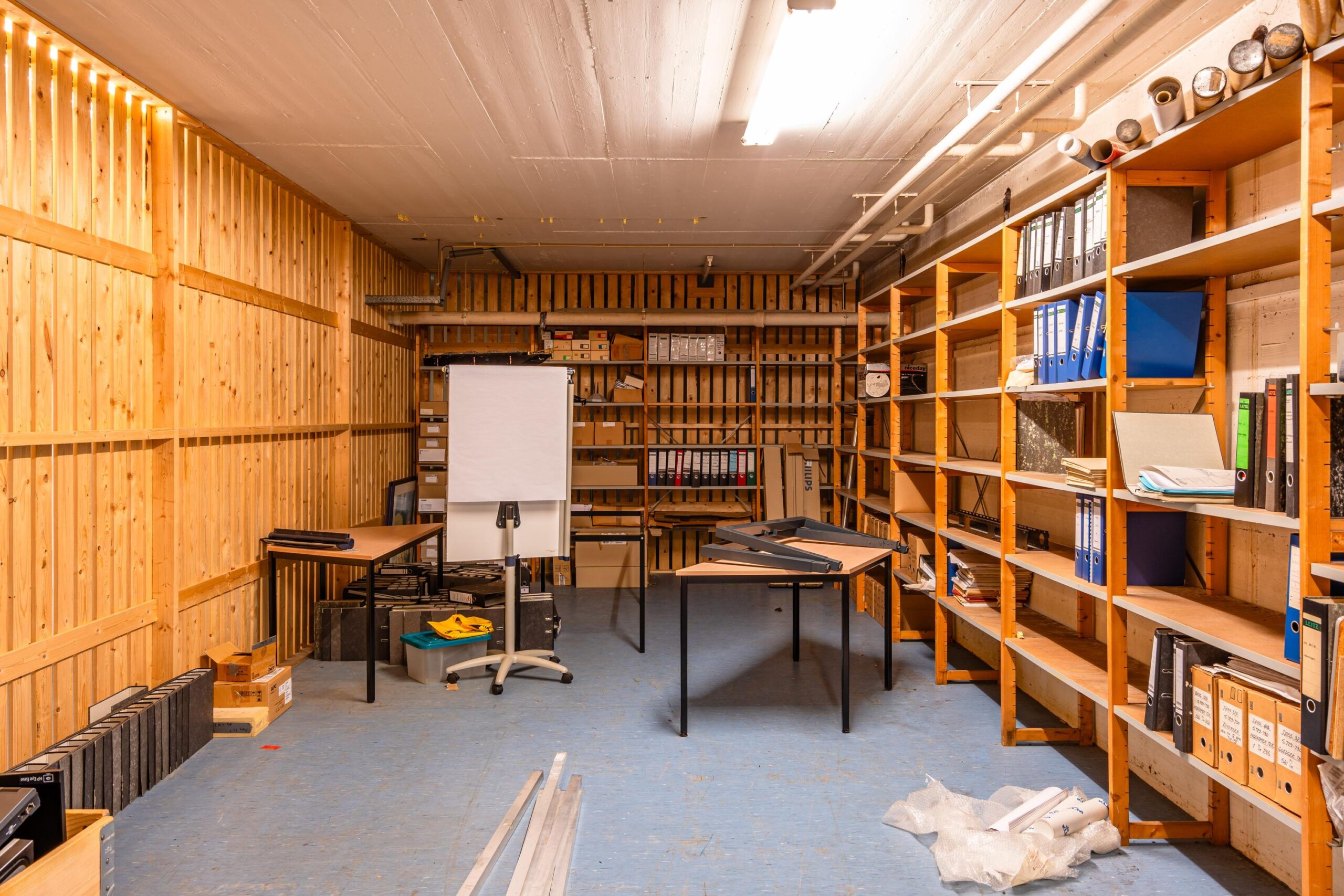 Een archiefkamer met houten planken vol mappen, dozen en een flipover.