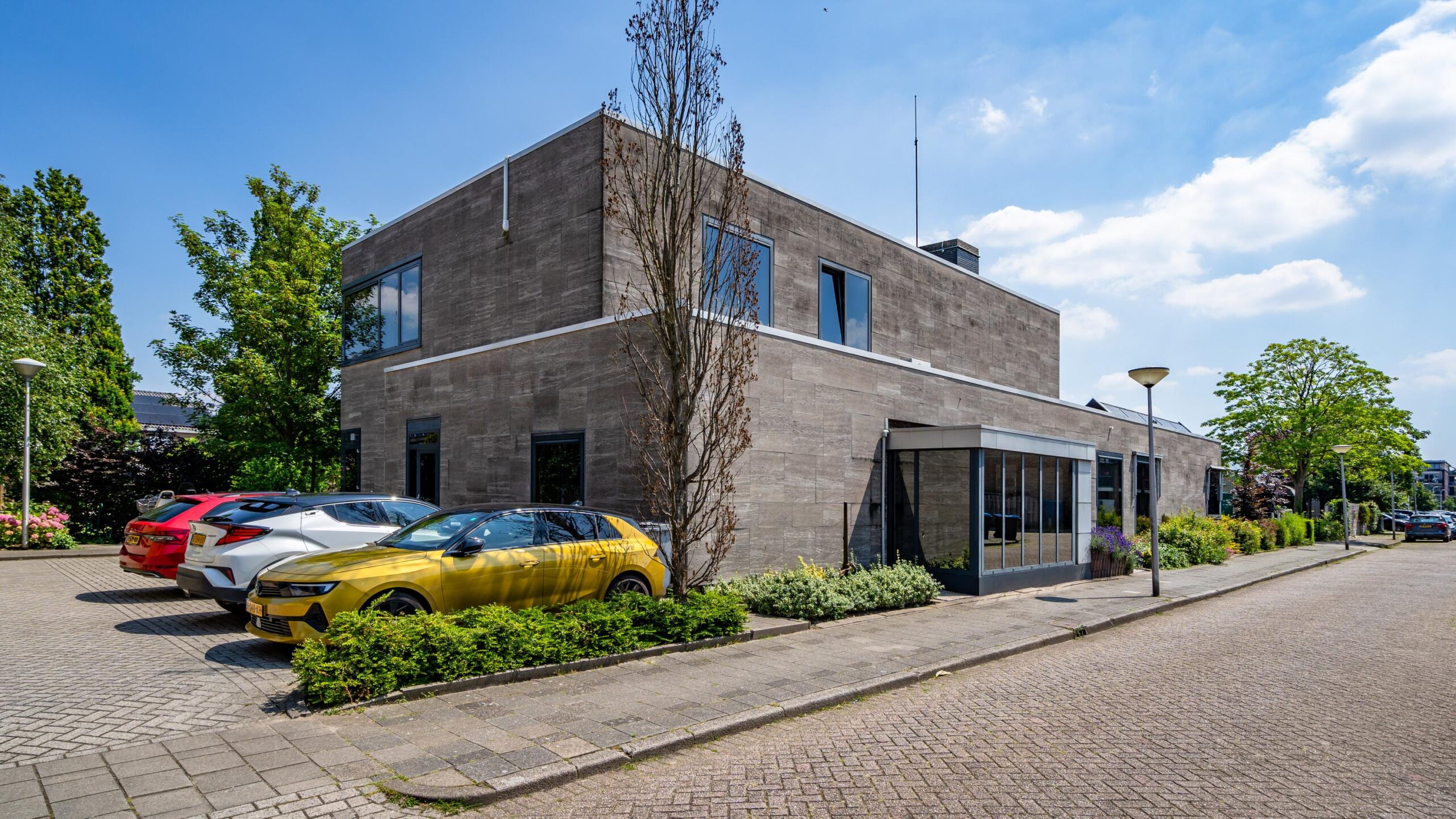 Een modern kantoorgebouw aan de Nicolaas Pieckstraat met geparkeerde auto's ervoor op een zonnige dag.