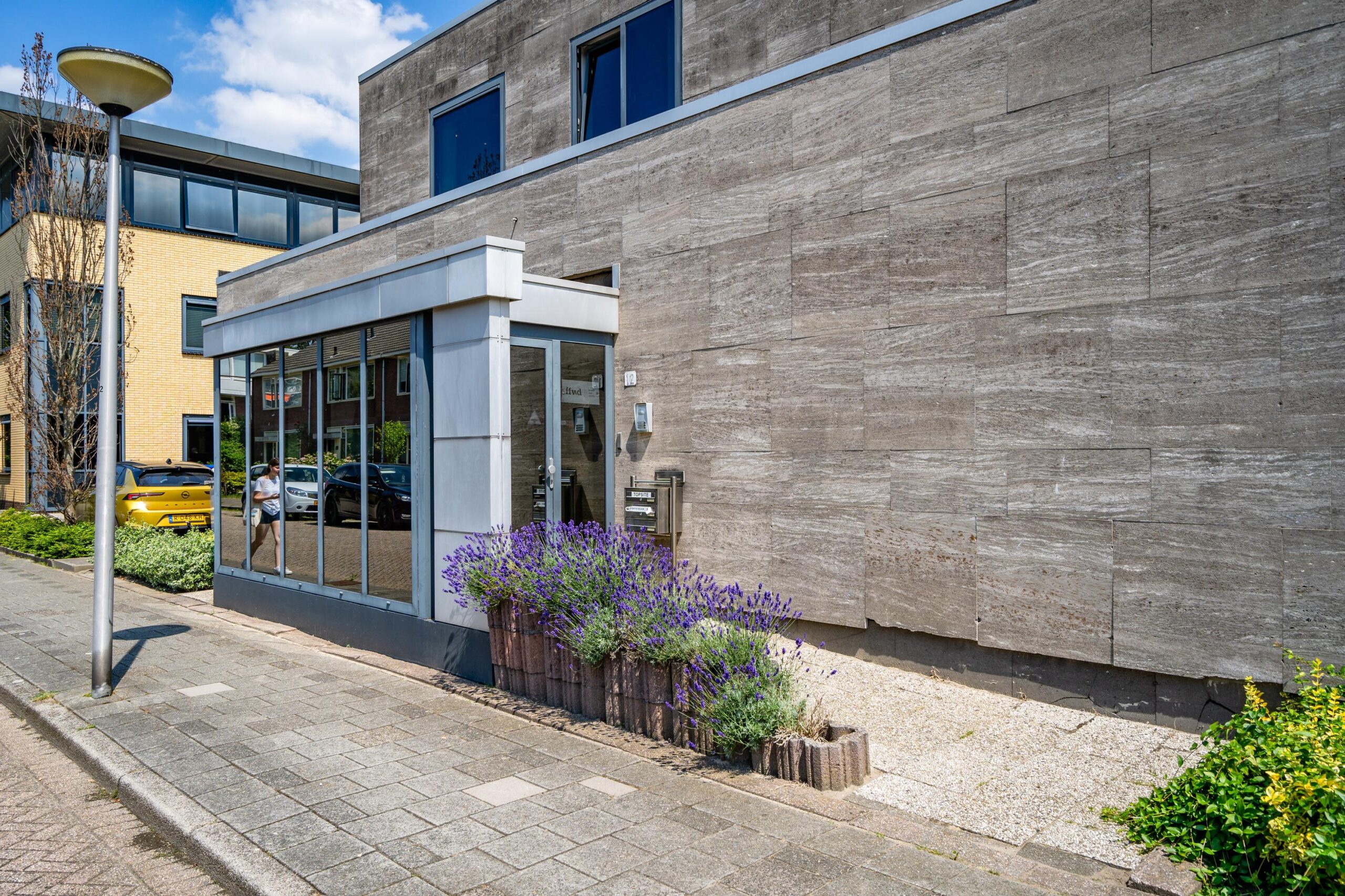 Een modern gebouw aan de Nicolaas Pieckstraat met een glazen ingang en paarse lavendel in de voortuin.
