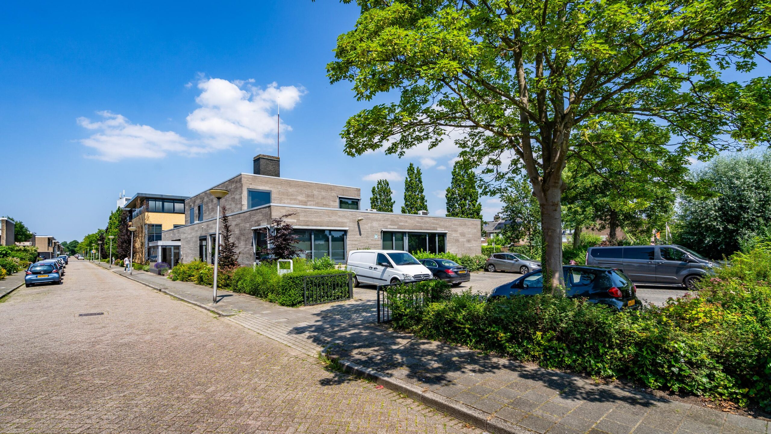 Een zonnige straat met moderne gebouwen aan de Nicolaas Pieckstraat, omgeven door groen en geparkeerde auto's.