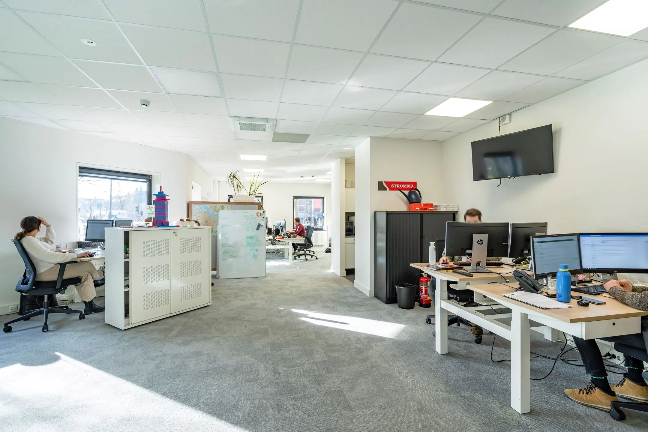 Een modern en licht kantoor met meerdere werkplekken waar mensen geconcentreerd aan het werk zijn.