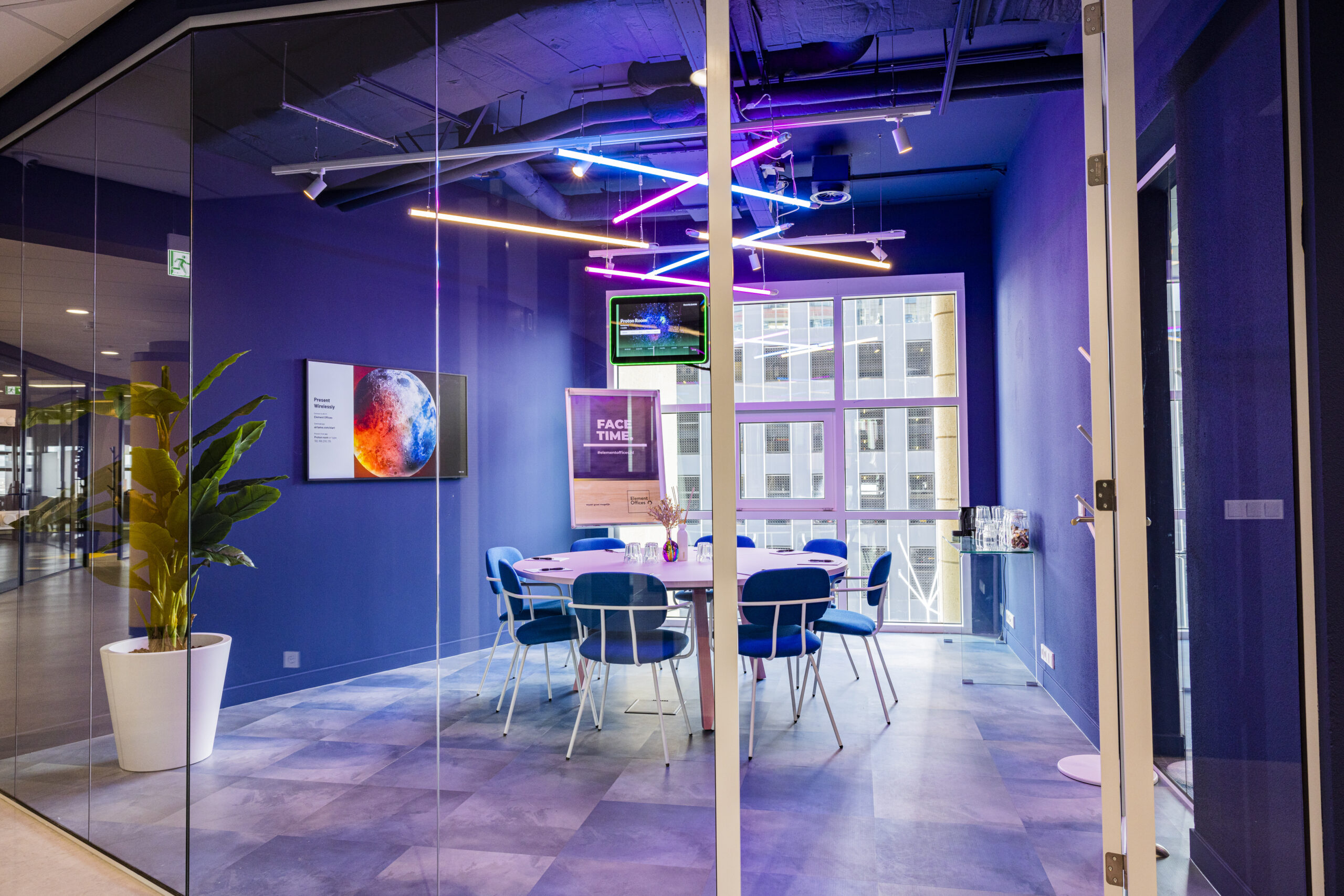 Een moderne vergaderruimte met blauwe muren, felgekleurde neonverlichting en een grote tafel omringd door stoelen.