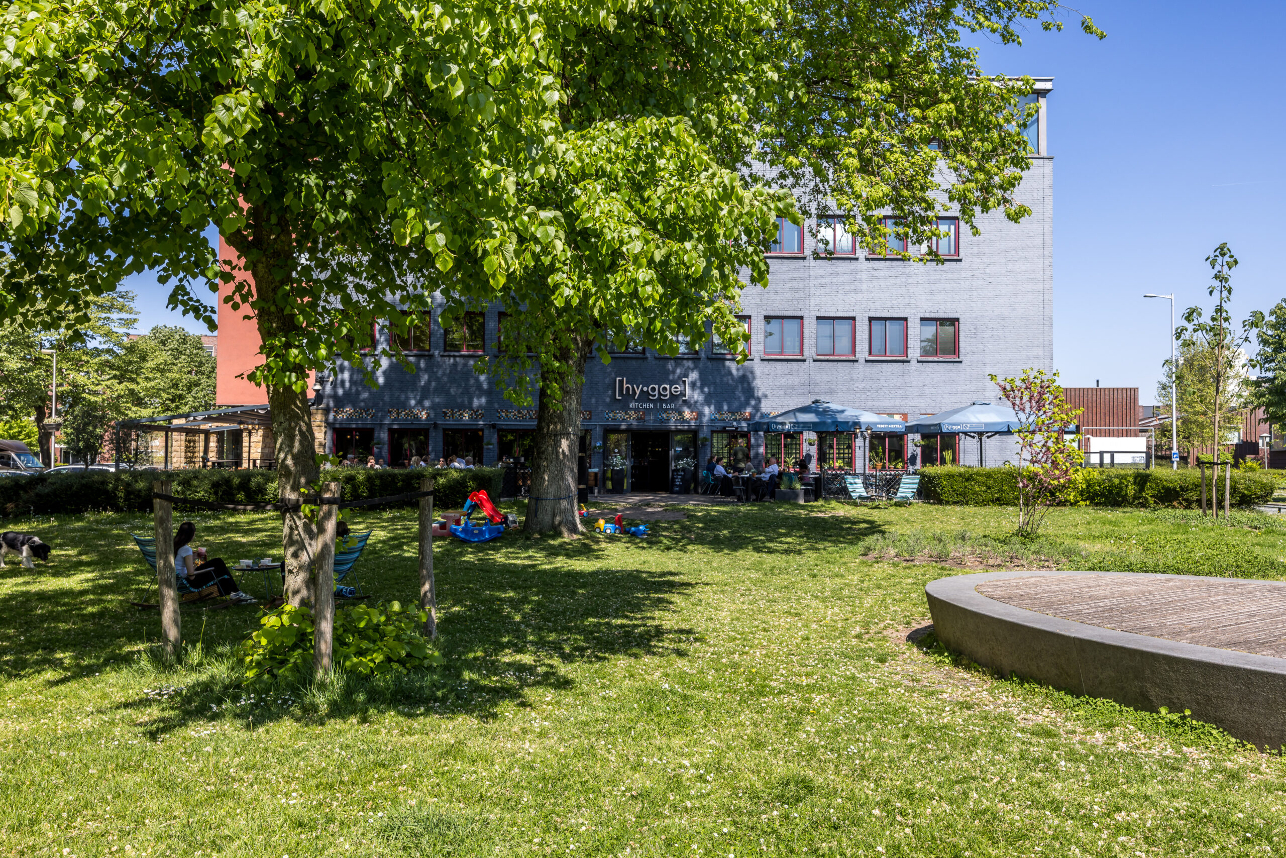 Een zonnig, groen park met mensen die ontspannen voor het [hy-gge] restaurant aan de Goeman Borgesiuslaan 77 in Utrecht.