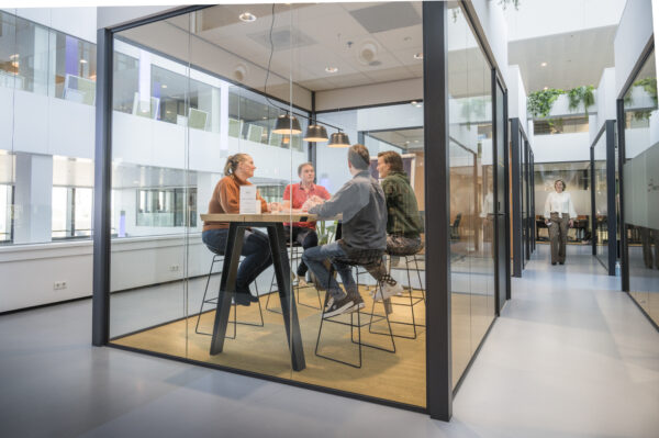 Een groep mensen zit te vergaderen in een moderne glazen vergaderruimte.