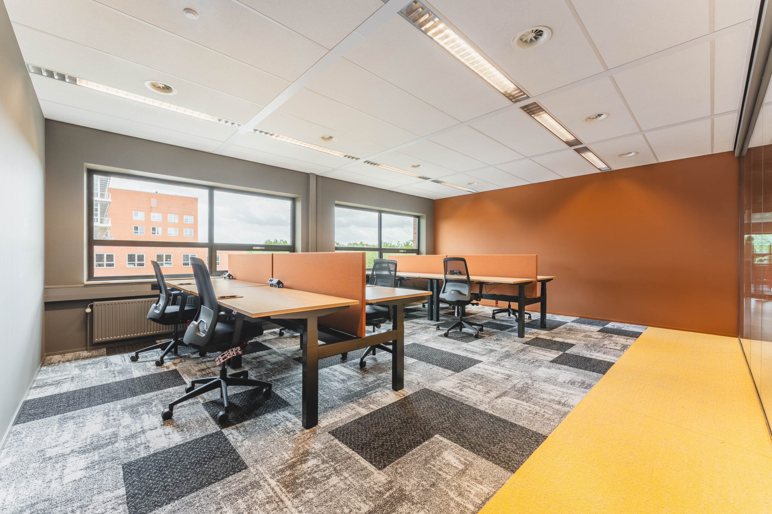 Een moderne, lichte kantoorruimte met bureaus, stoelen en een oranje accentmuur.