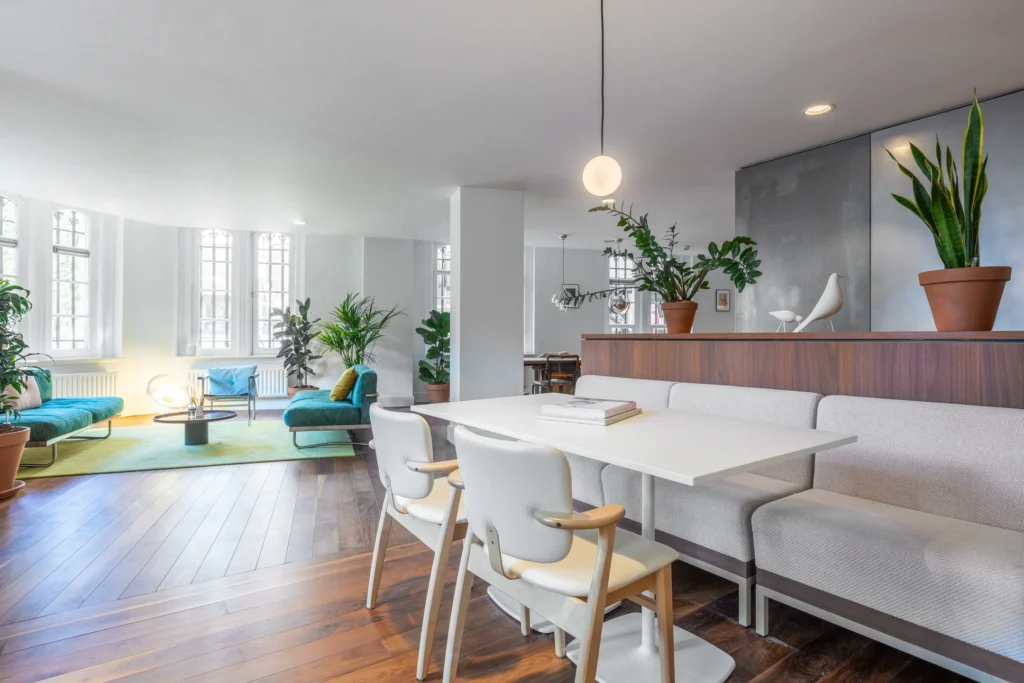 Lichte en moderne woonkamer met houten vloer, planten en minimalistische meubels.