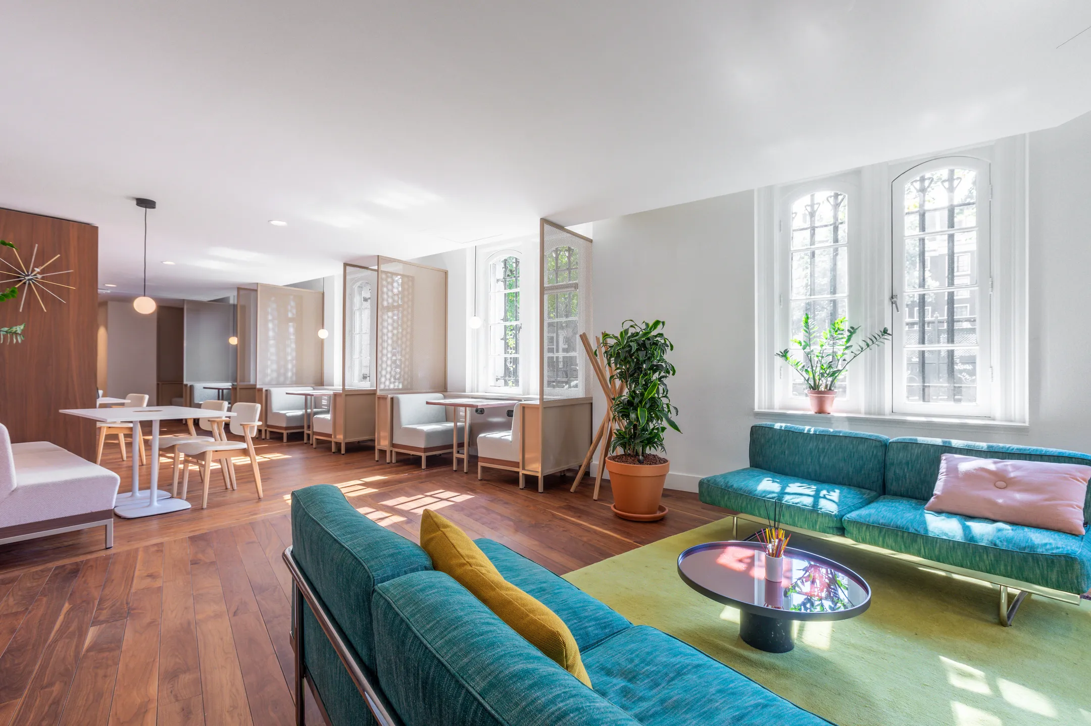 Moderne lounge- en eetruimte met houten vloeren, groene banken en veel natuurlijk licht.