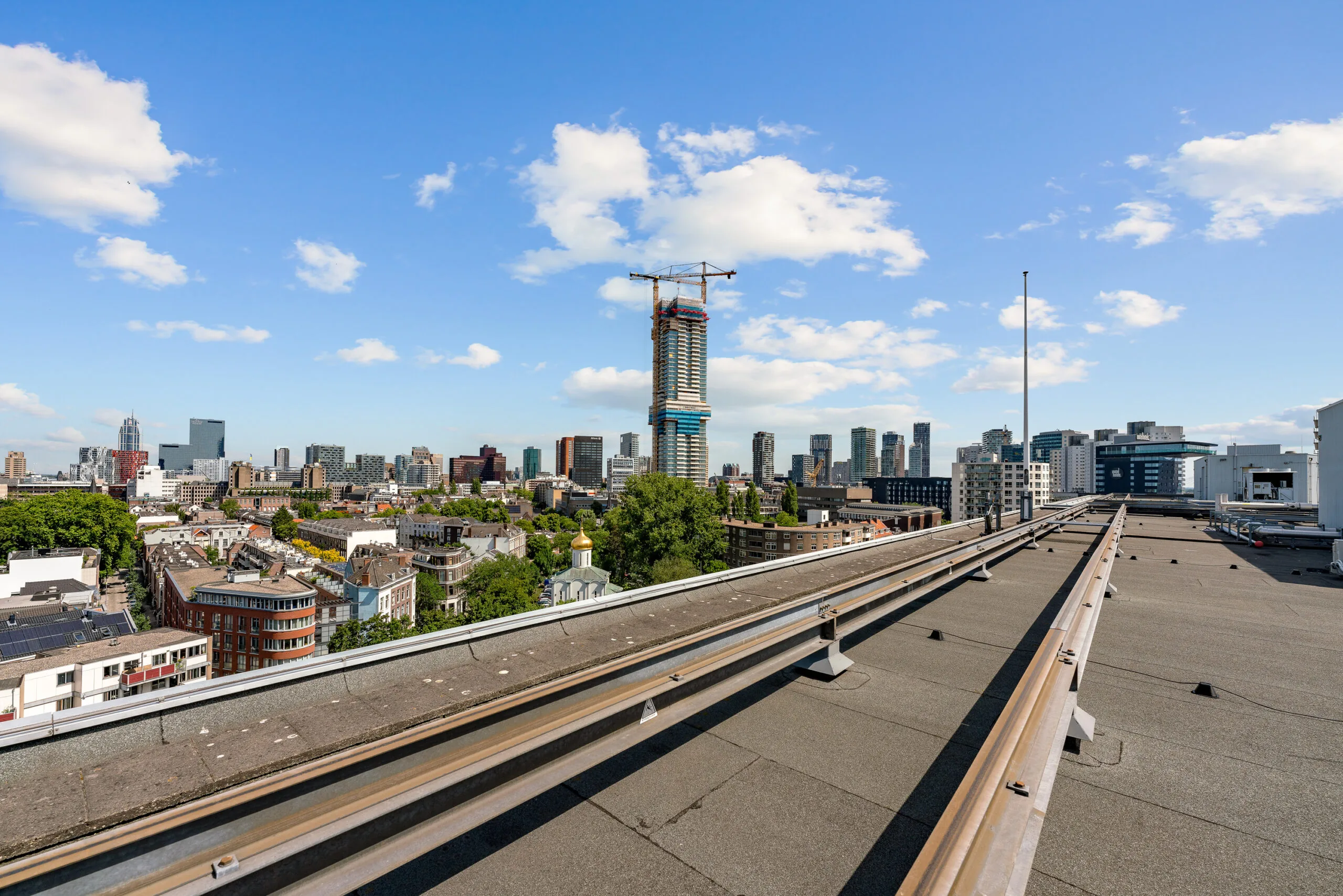 Uitzicht vanaf een dak op de skyline van Rotterdam met een in aanbouw zijnde wolkenkrabber in het midden.
