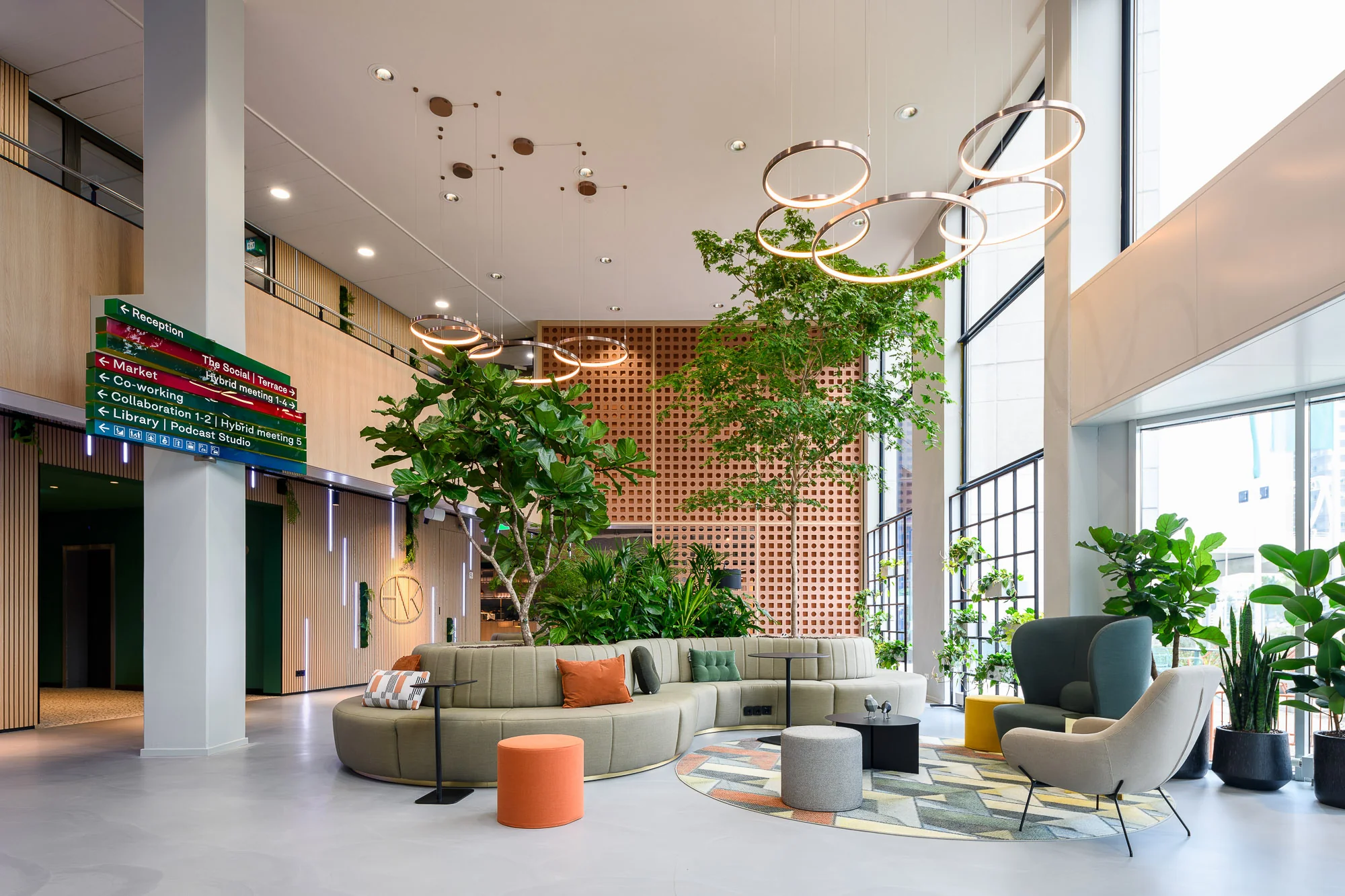 Moderne, lichtovergoten lounge- en werkruimte met groen meubilair, planten en decoratieve verlichting.