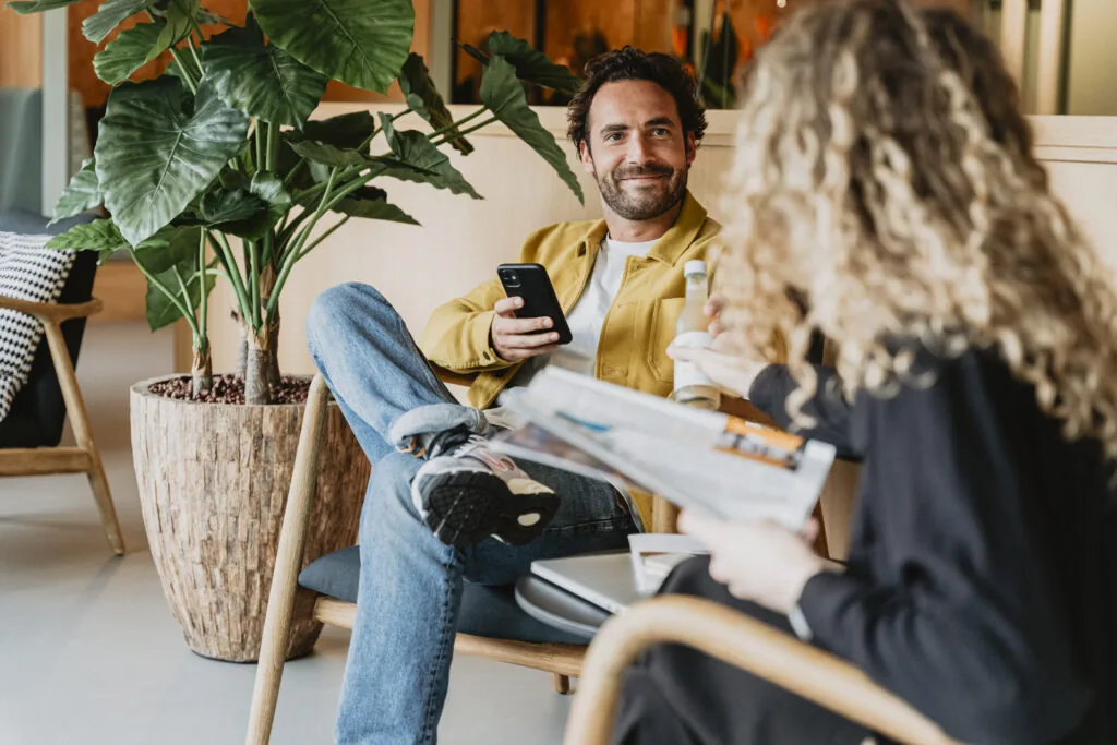 Twee mensen zitten ontspannen in een loungehoek van HNK Amsterdam Schinkel 2, terwijl ze praten en iets drinken.