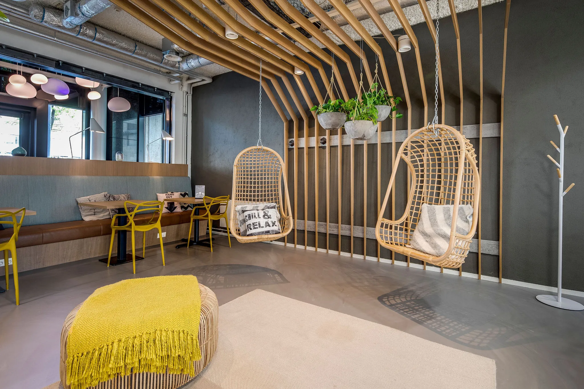 Moderne loungehoek in HNK Rotterdam Centrum met hangstoelen, gele accenten en houten designpanelen.