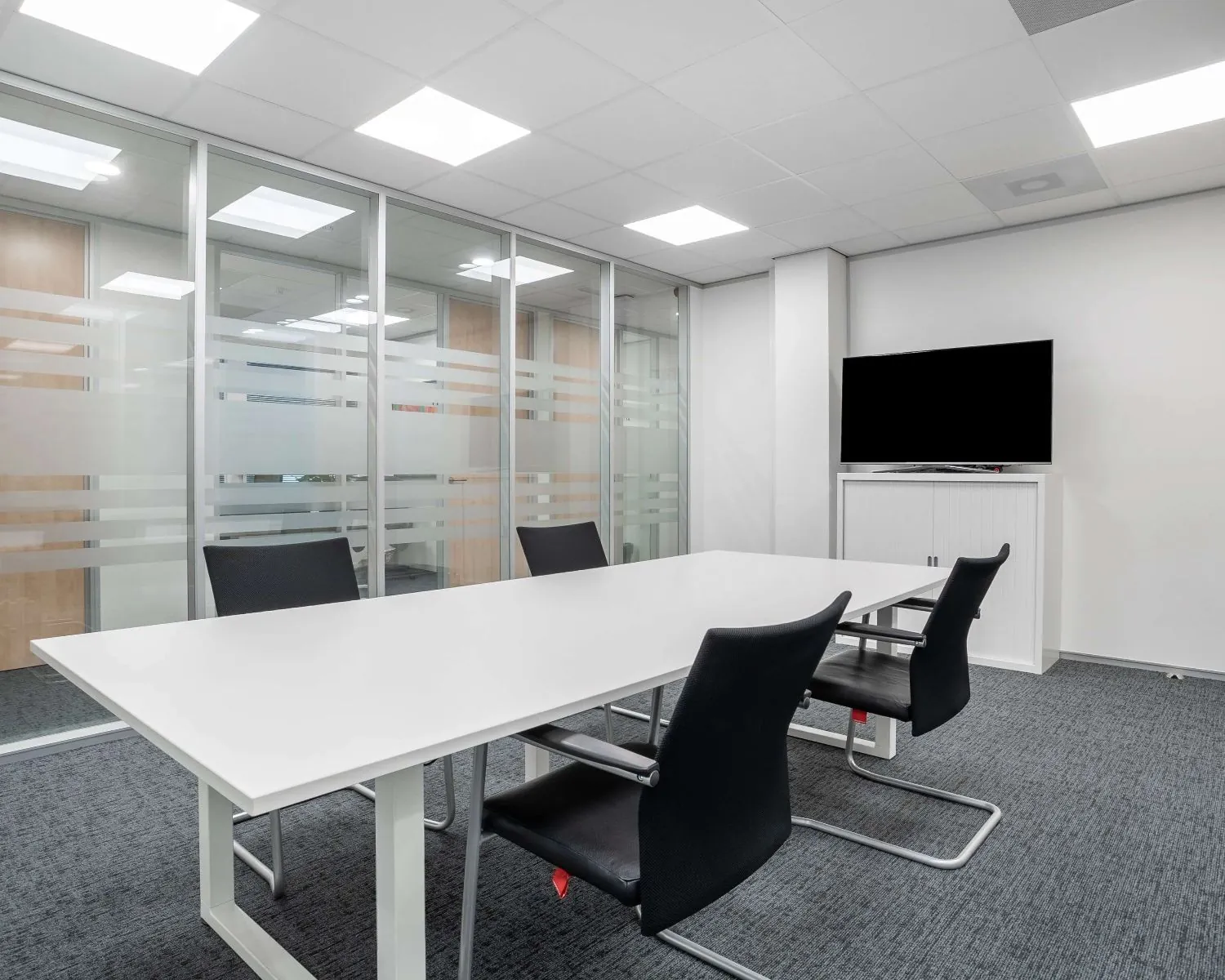 Moderne vergaderruimte met glazen wanden, een witte tafel, zwarte stoelen en een flatscreen-tv in een kantoor aan de Hurksestraat 43 in Eindhoven.
