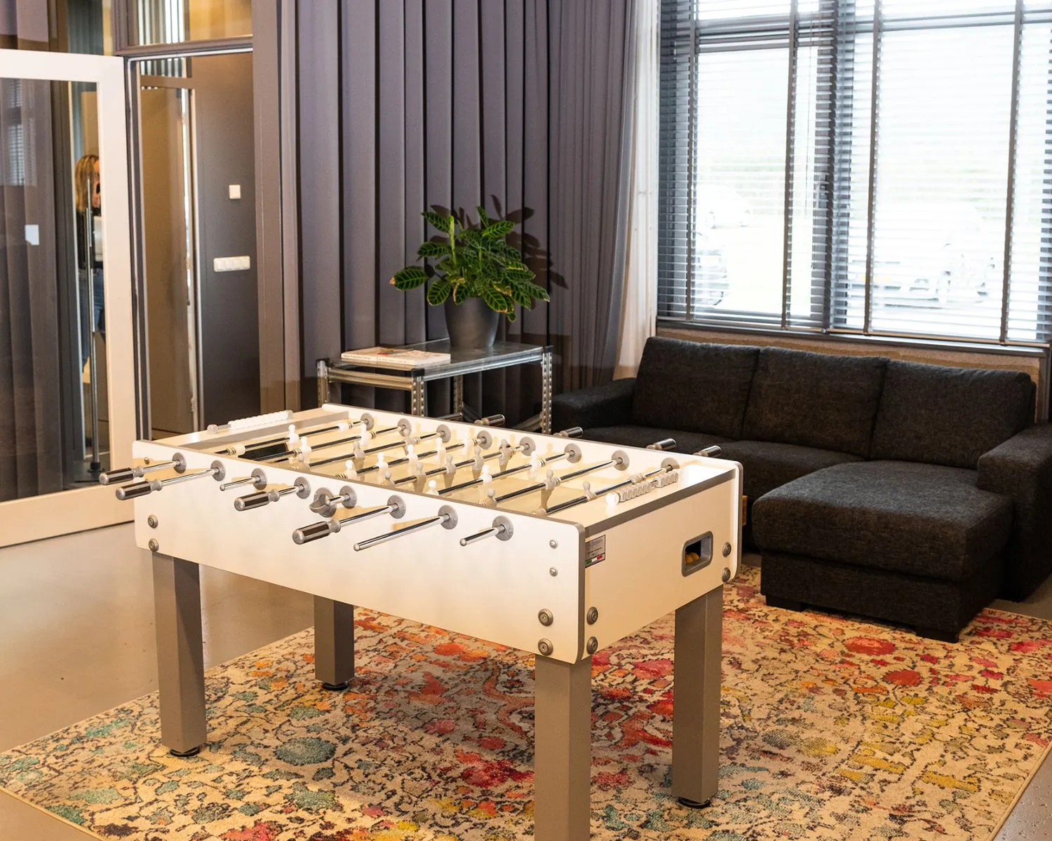 Moderne loungeruimte in een kantoor aan de Bolderweg 2 in Almere met een tafelvoetbaltafel, bank en kleurrijk vloerkleed.