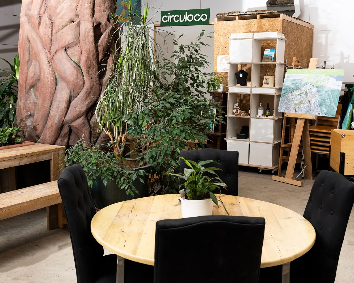 Ronde houten vergadertafel met planten, omringd door zwarte stoelen in een groene kantoorruimte bij Steiger 24 in Almere.