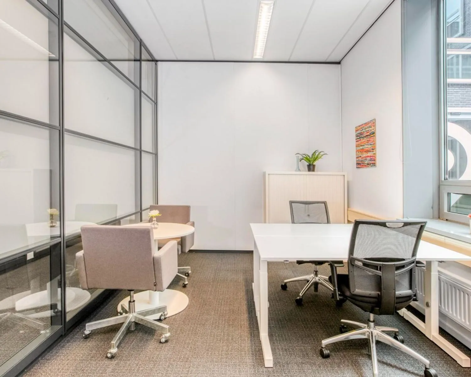 Moderne kantoorruimte met glazen wand, twee bureaus en vergadertafel in Flight Forum 40 in Eindhoven.