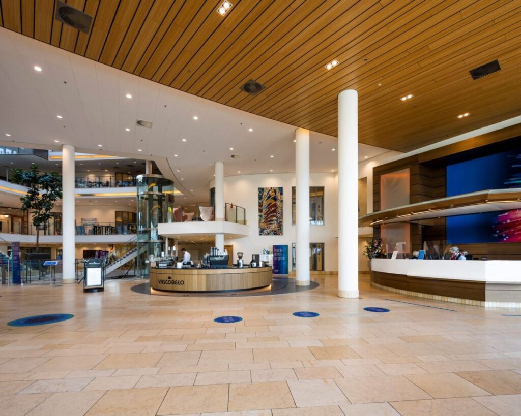 Moderne lobby van een kantoorpand aan de Laan van Langerhuizen 1 in Amstelveen met een receptiebalie, café en glazen lift.