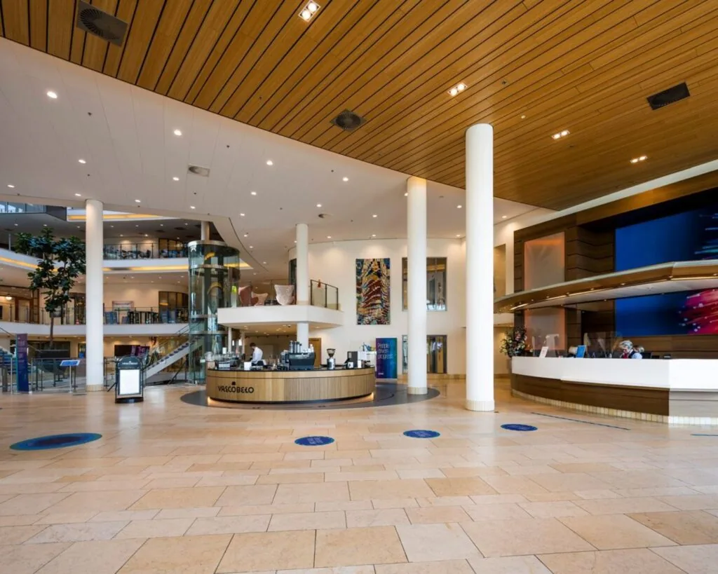 Moderne lobby van een kantoorpand aan de Laan van Langerhuizen 1 in Amstelveen met een receptiebalie, café en glazen lift.