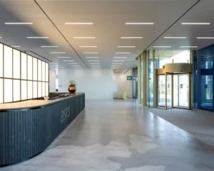 Moderne en ruime entreehal van een kantoorpand aan de Taurusavenue 165 in Hoofddorp met een receptiebalie van ASICS en een glazen draaideur.