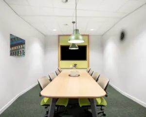Moderne vergaderruimte met een lange houten tafel, acht stoelen en groene accenten in Capitool 10, Enschede.
