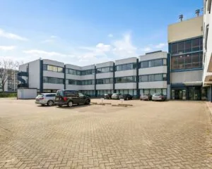 Voorgevel van een modern kantoorgebouw aan de Hooilaan 1 in Breda met parkeerplaatsen op een ruim parkeerterrein.