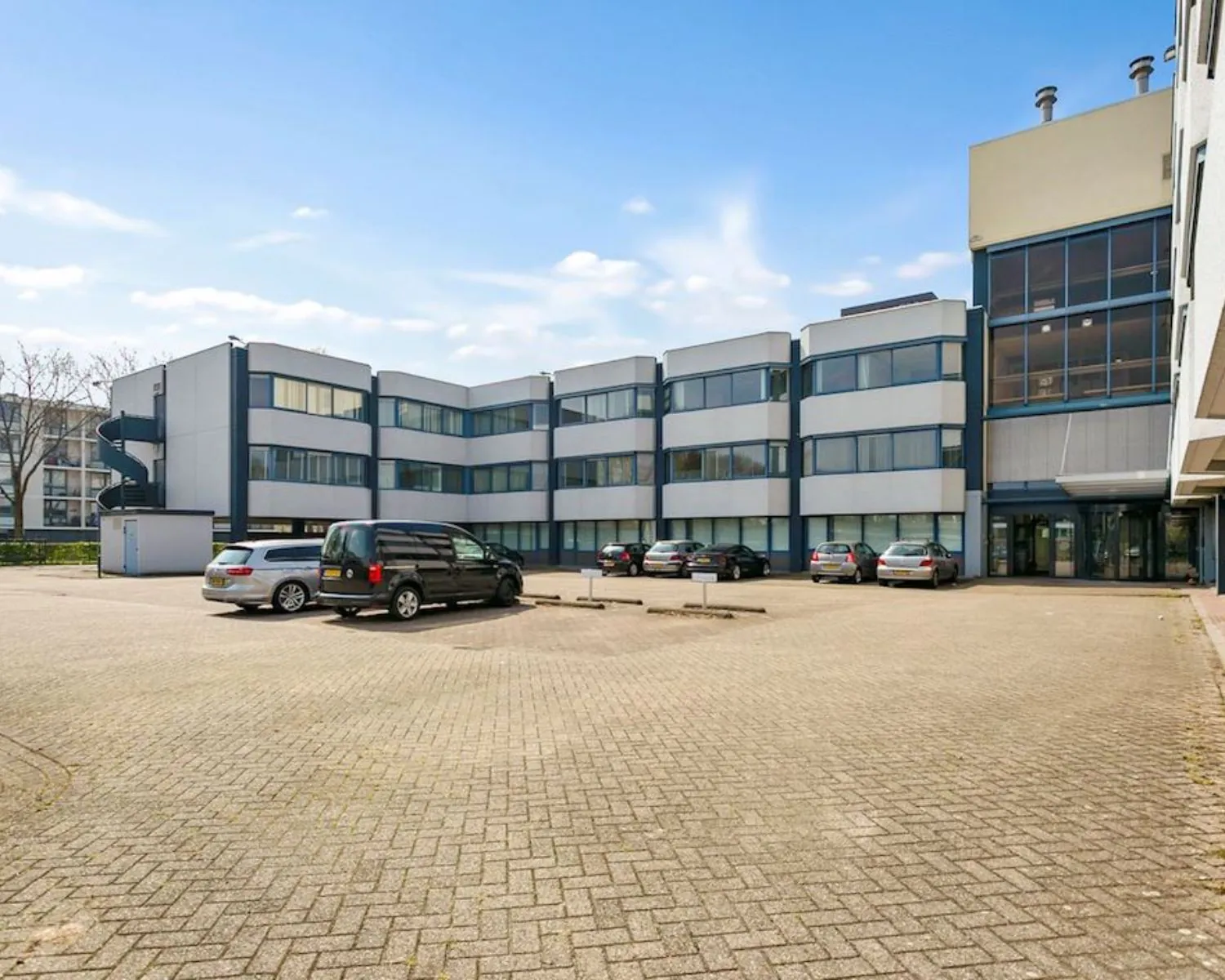 Voorgevel van een modern kantoorgebouw aan de Hooilaan 1 in Breda met parkeerplaatsen op een ruim parkeerterrein.