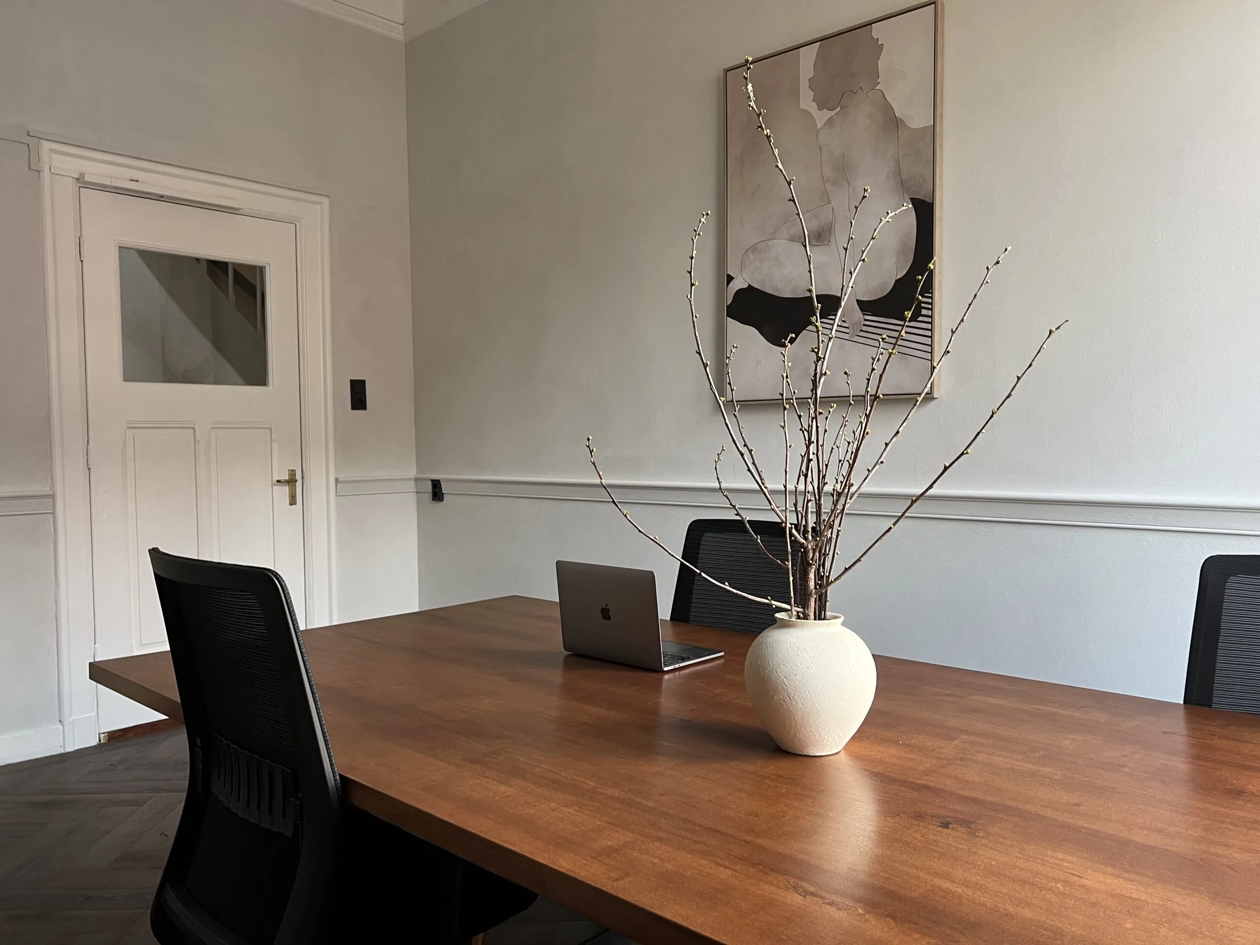 Vergaderruimte bij Creativegrounds Emmalaan met houten tafel, laptop, vaas met takken en kunst aan de muur.