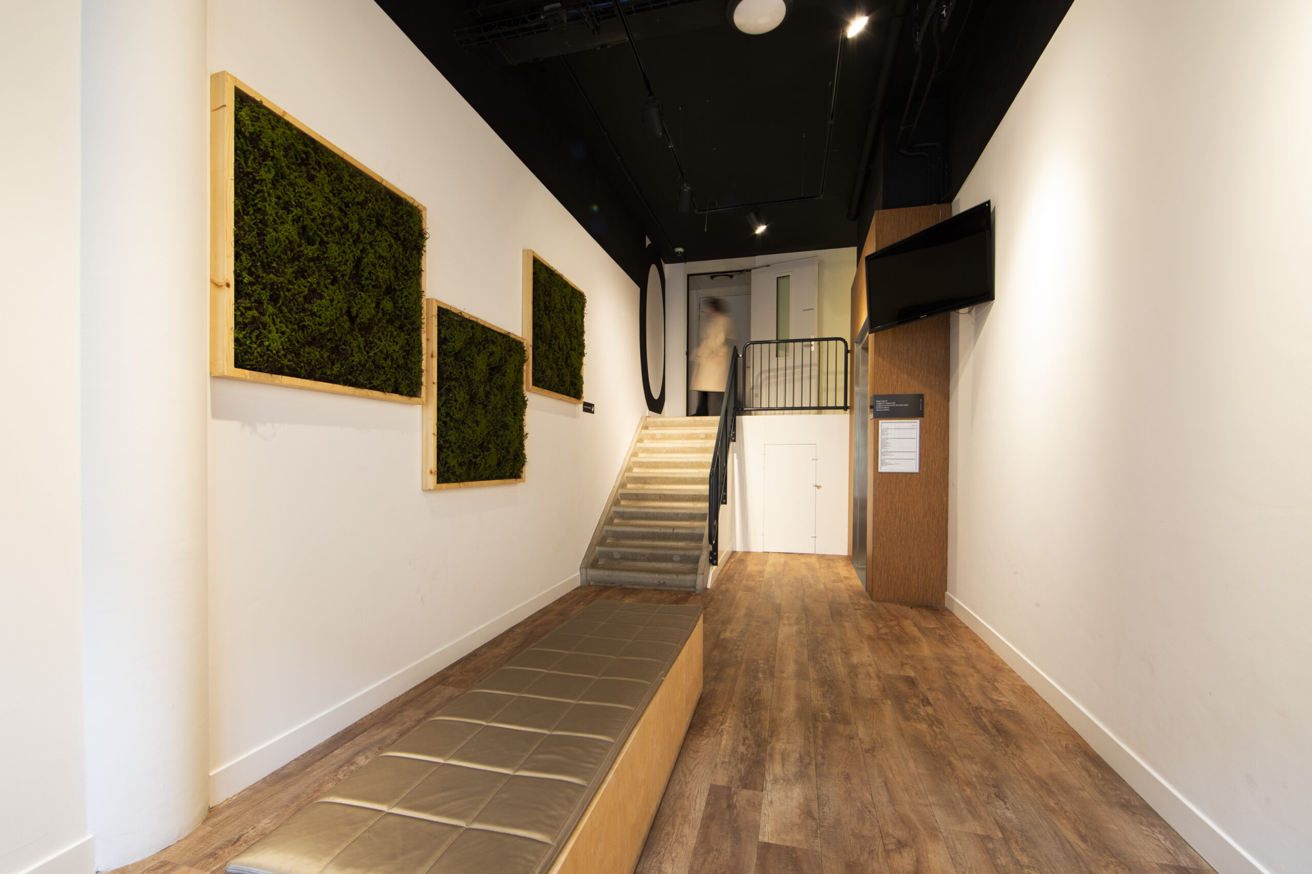 Entreehal met houten vloer, groene mospanelen aan de muur en een trap naar boven.