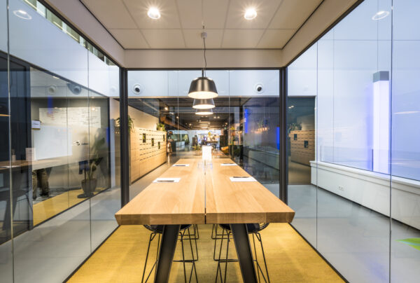 Een moderne vergaderruimte met glazen wanden en een lange houten tafel, verlicht door hanglampen.