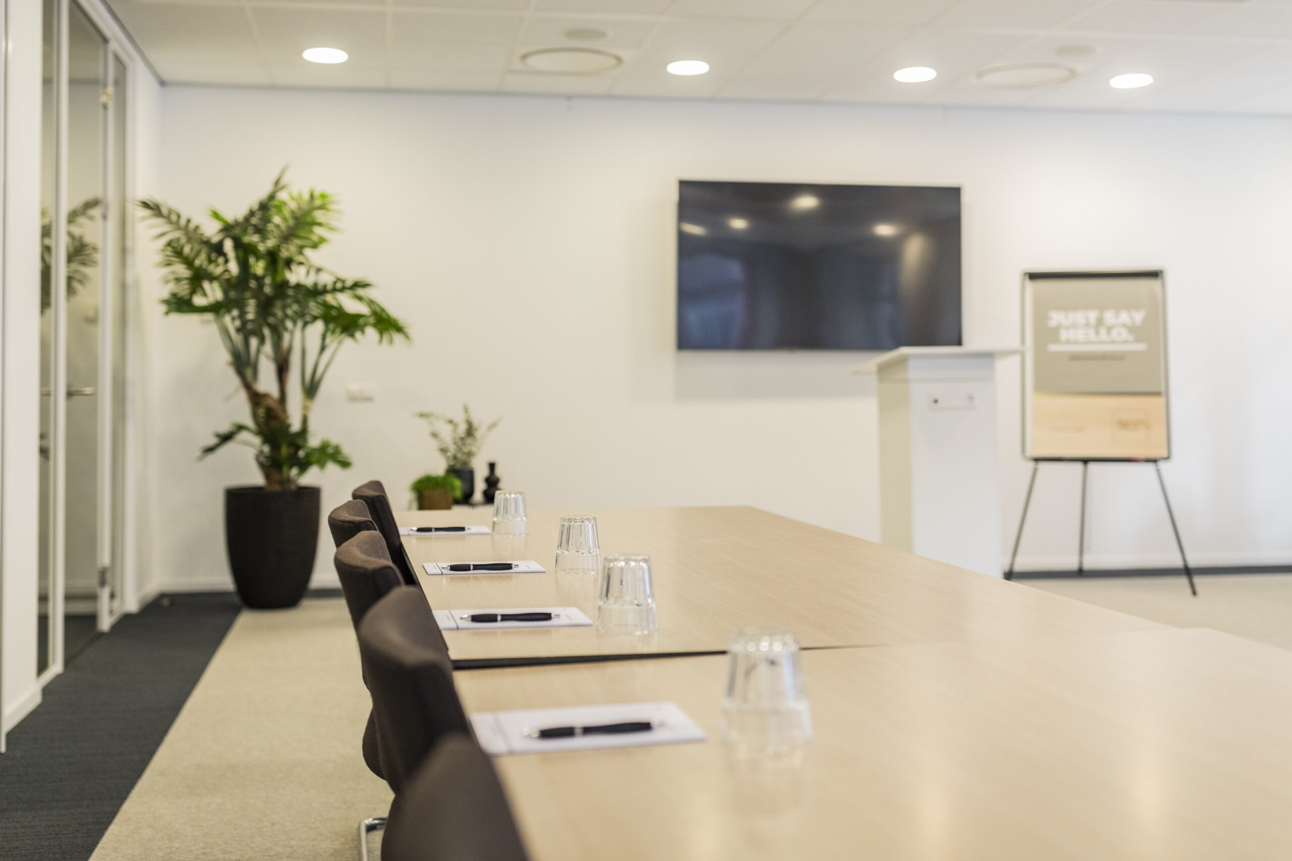 Een moderne vergaderruimte met een lange tafel, opgestelde stoelen, een groot scherm en een flip-over.