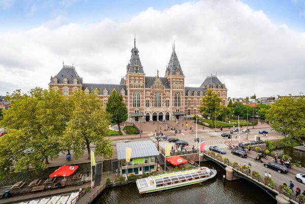 Voorgevel van het Rijksmuseum in Amsterdam met een rondvaartboot op de gracht op de voorgrond.