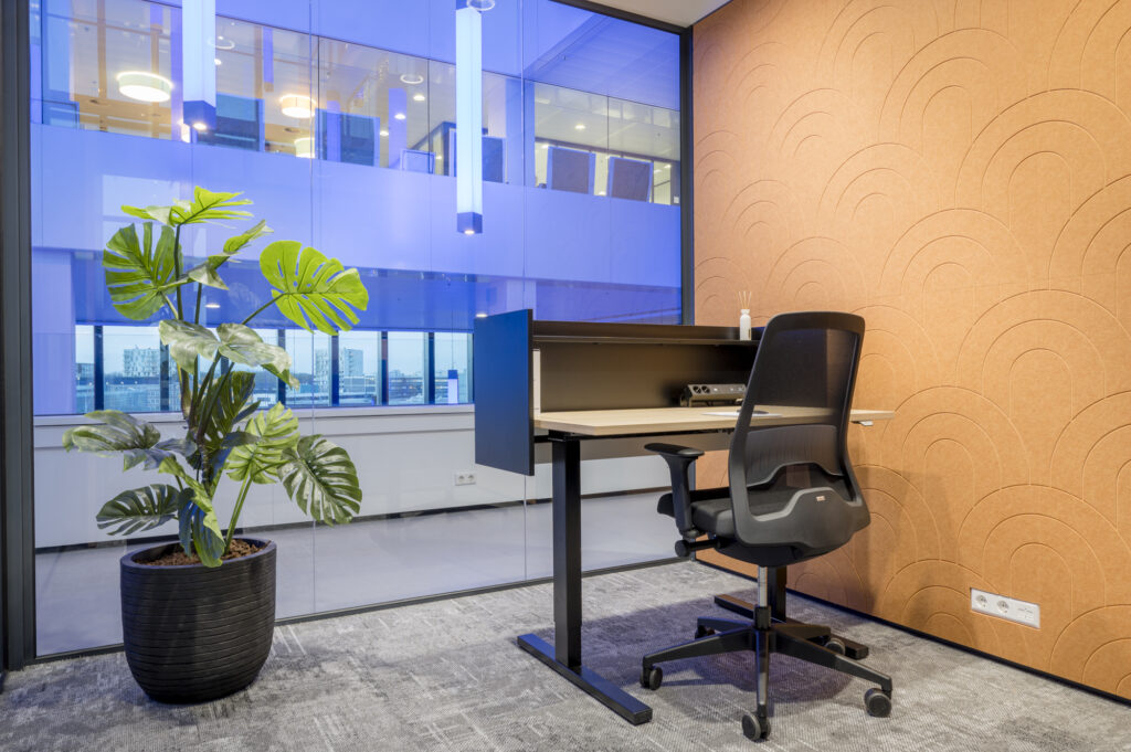 Kleine moderne kantoorruimte met een zwart bureau, ergonomische stoel, kamerplant en oranje wanddecoratie.