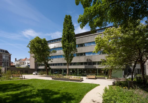 Een modern gebouw omringd door groene bomen en een grasveld op een zonnige dag.