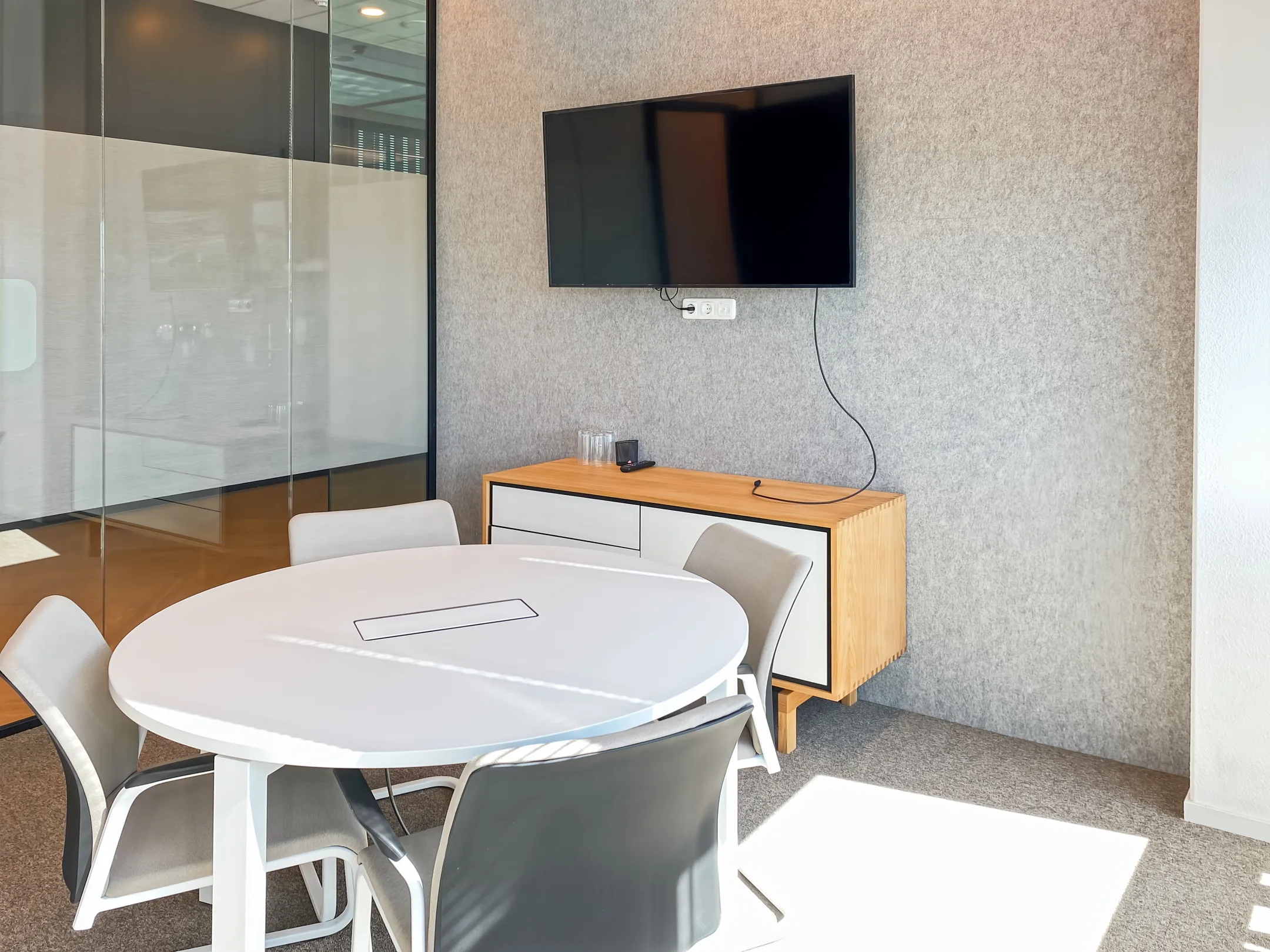 Vergaderruimte met een ronde tafel, vier stoelen, een wandkast en een tv aan de muur.