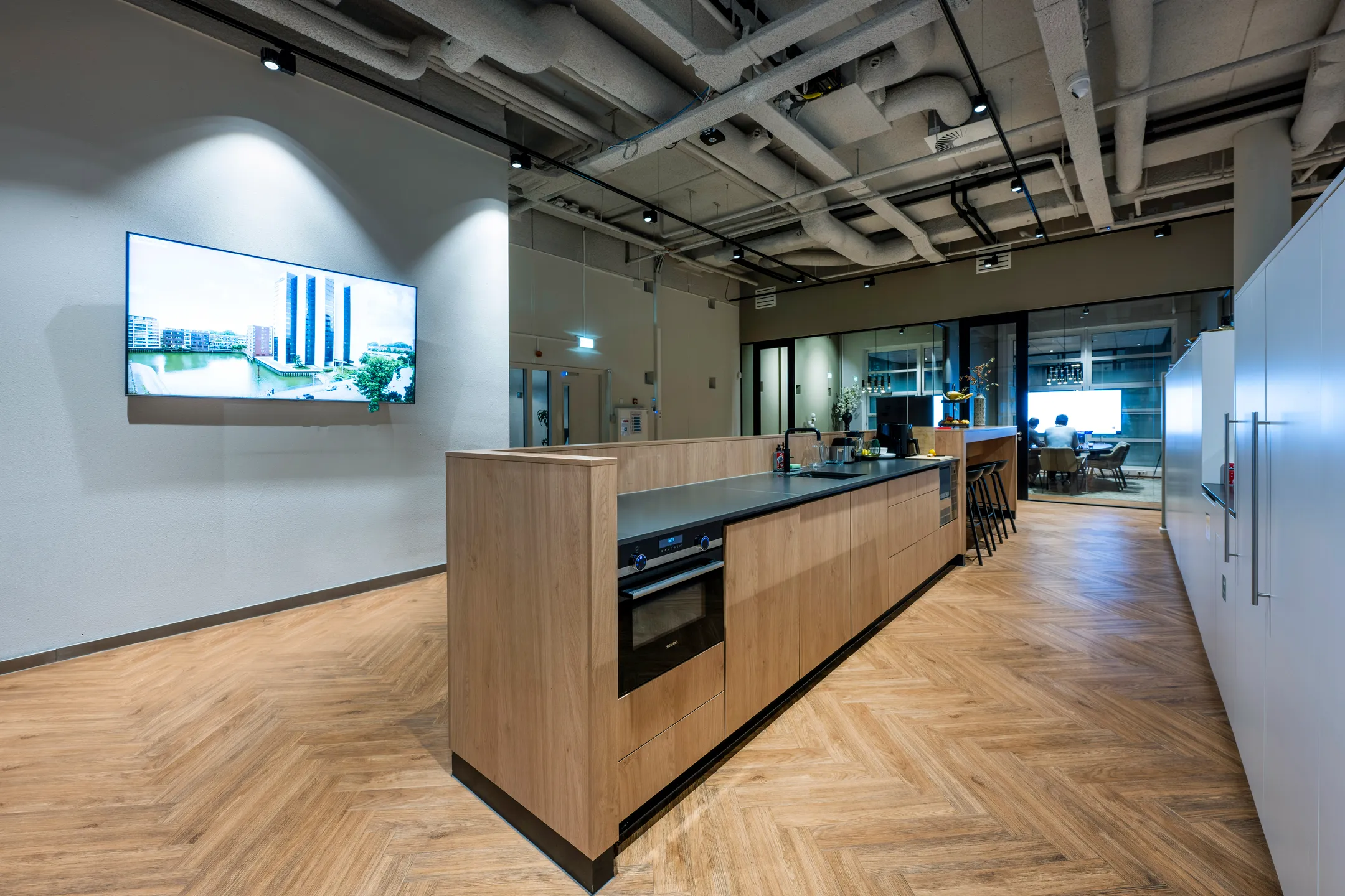 Een moderne kantoorruimte met een keuken, een vergaderruimte en een groot scherm aan de muur.