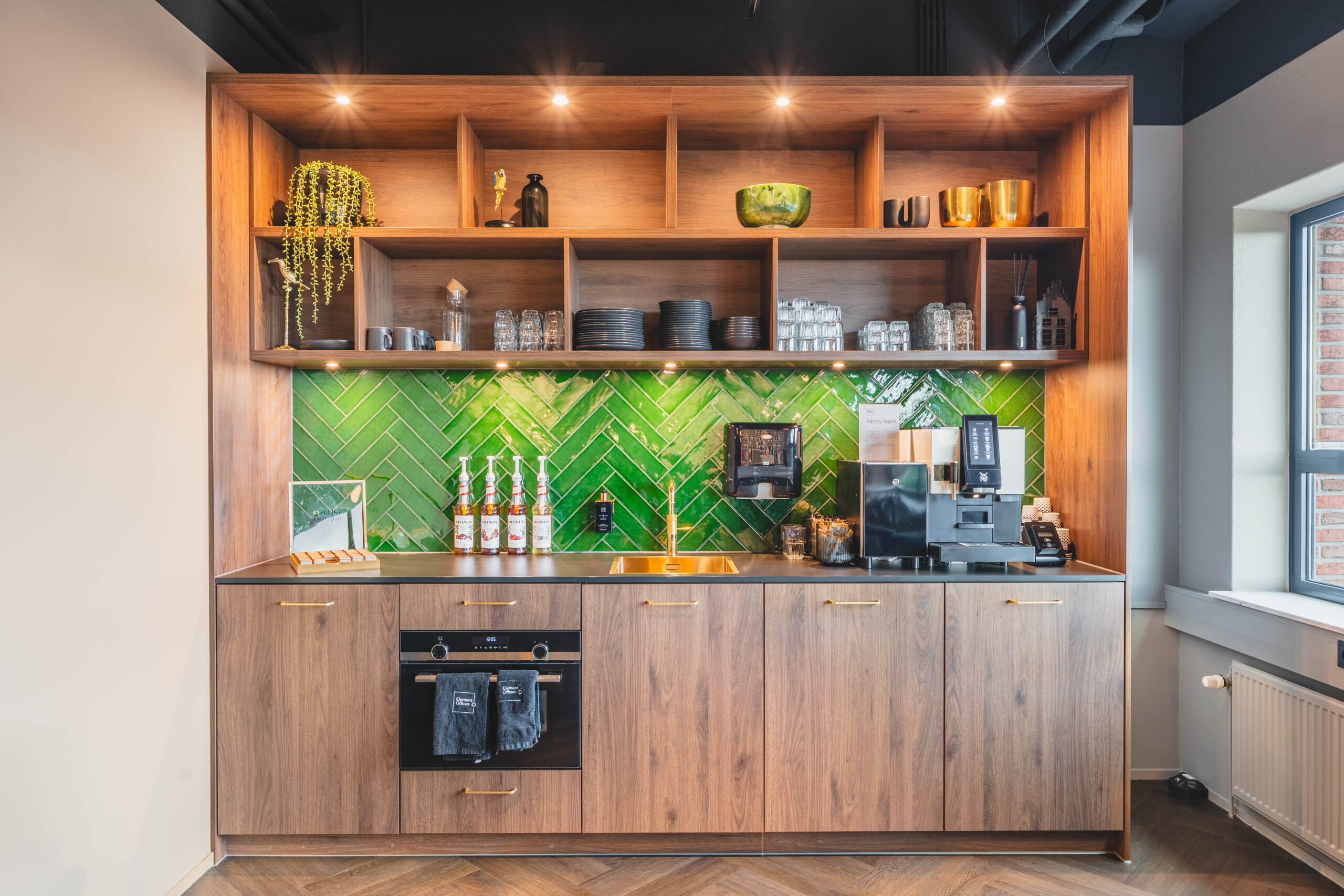 Modern keukenblok in hout met groene tegelachterwand en koffiemachine.