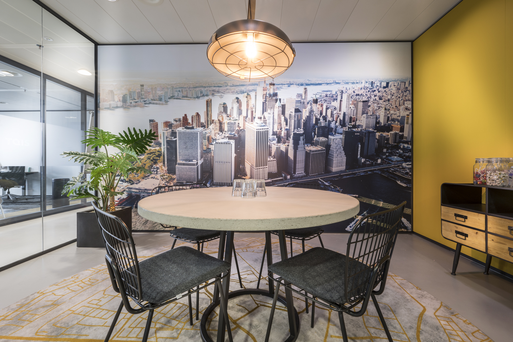 Stijlvolle vergaderruimte met een ronde tafel, draadstoelen, grote stadsfoto en sfeerverlichting.