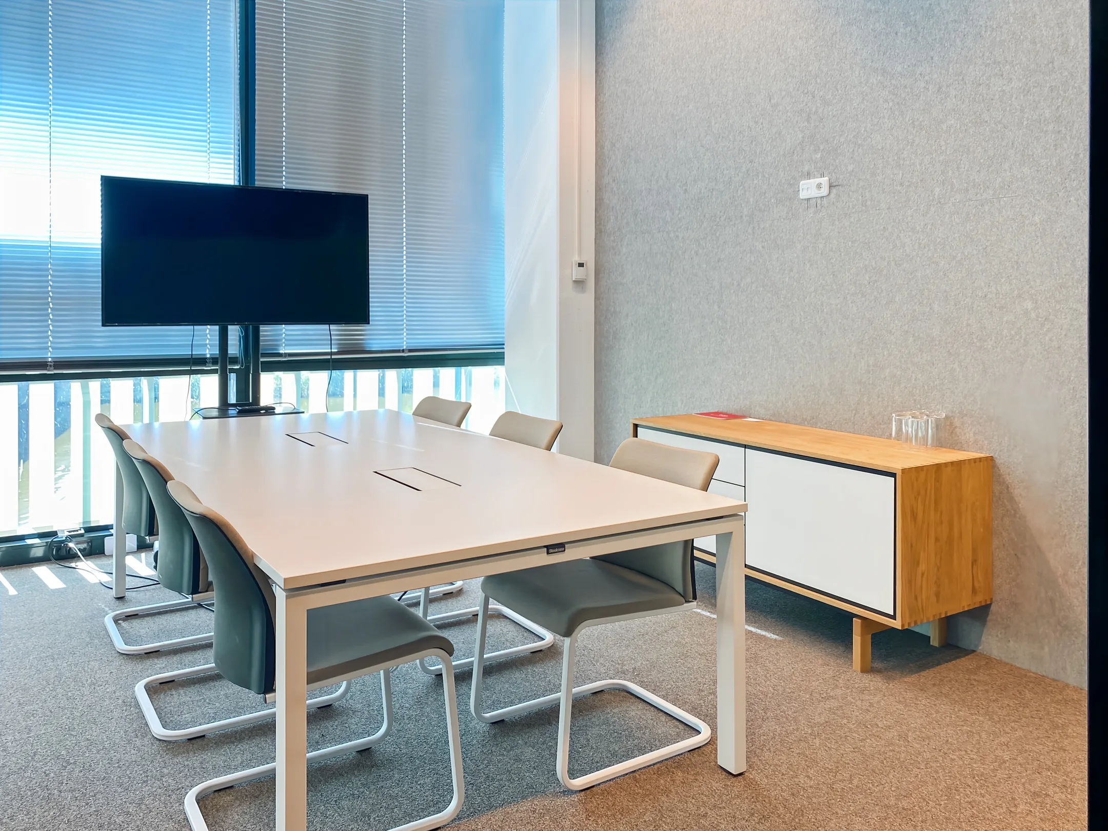 Een moderne vergaderruimte met een lange tafel, stoelen en een groot scherm.