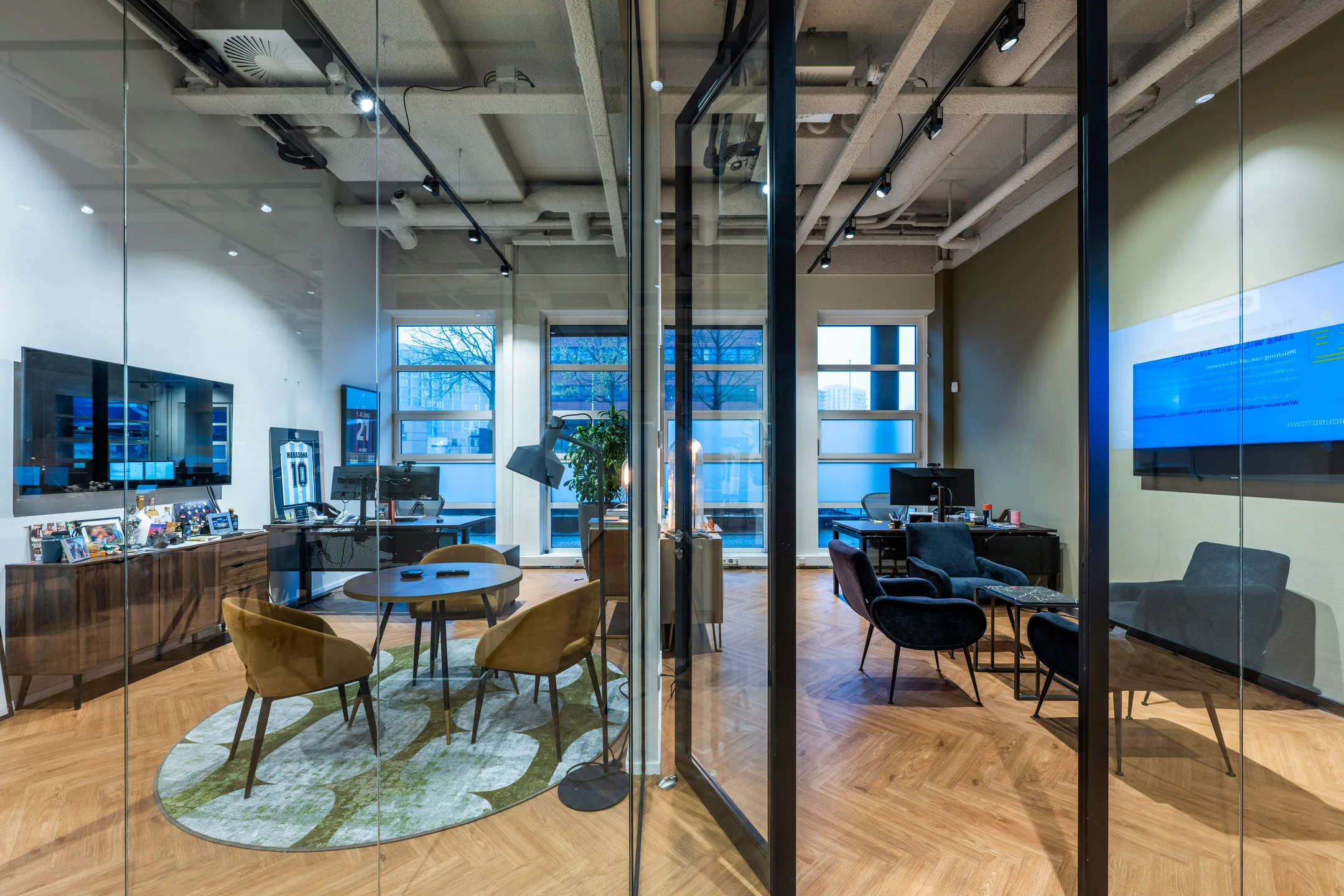 Moderne kantoorruimte met glazen wanden, ingericht met stoelen, tafels en enkele computerschermen.