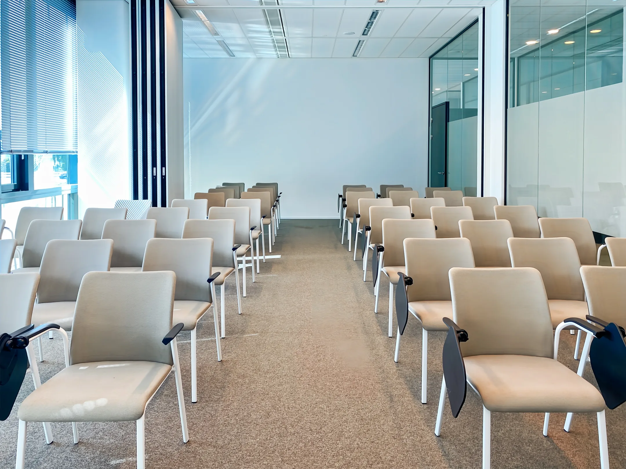 Rijen met lege beige stoelen in een moderne conferentieruimte.