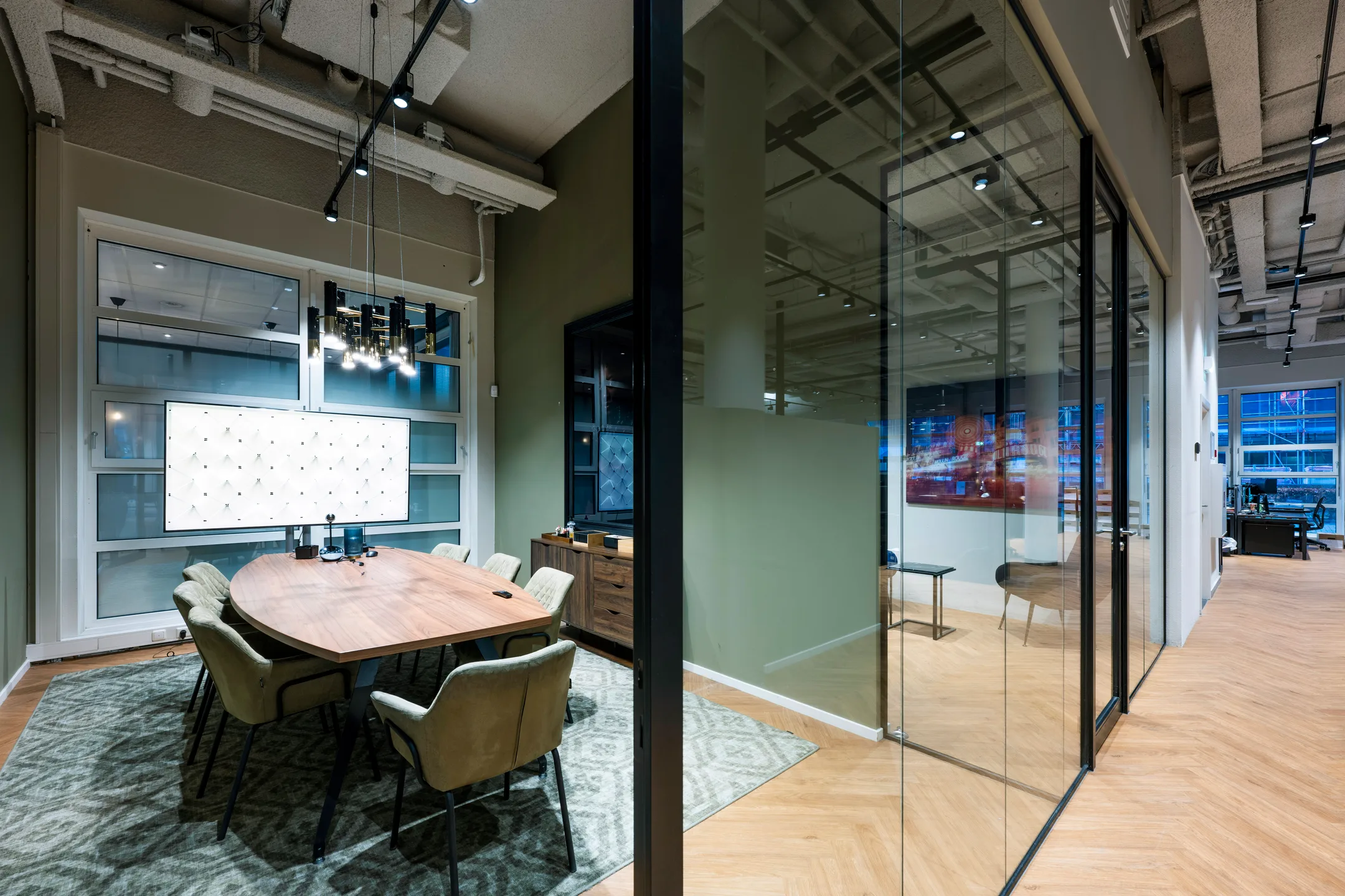 Een moderne vergaderruimte met een houten tafel en comfortabele stoelen, gescheiden van de gang door glazen wanden.