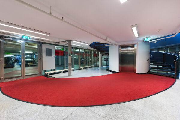 Hal met rode vloerbedekking bij de lift en wenteltrap in parkeergarage Herculesplein.