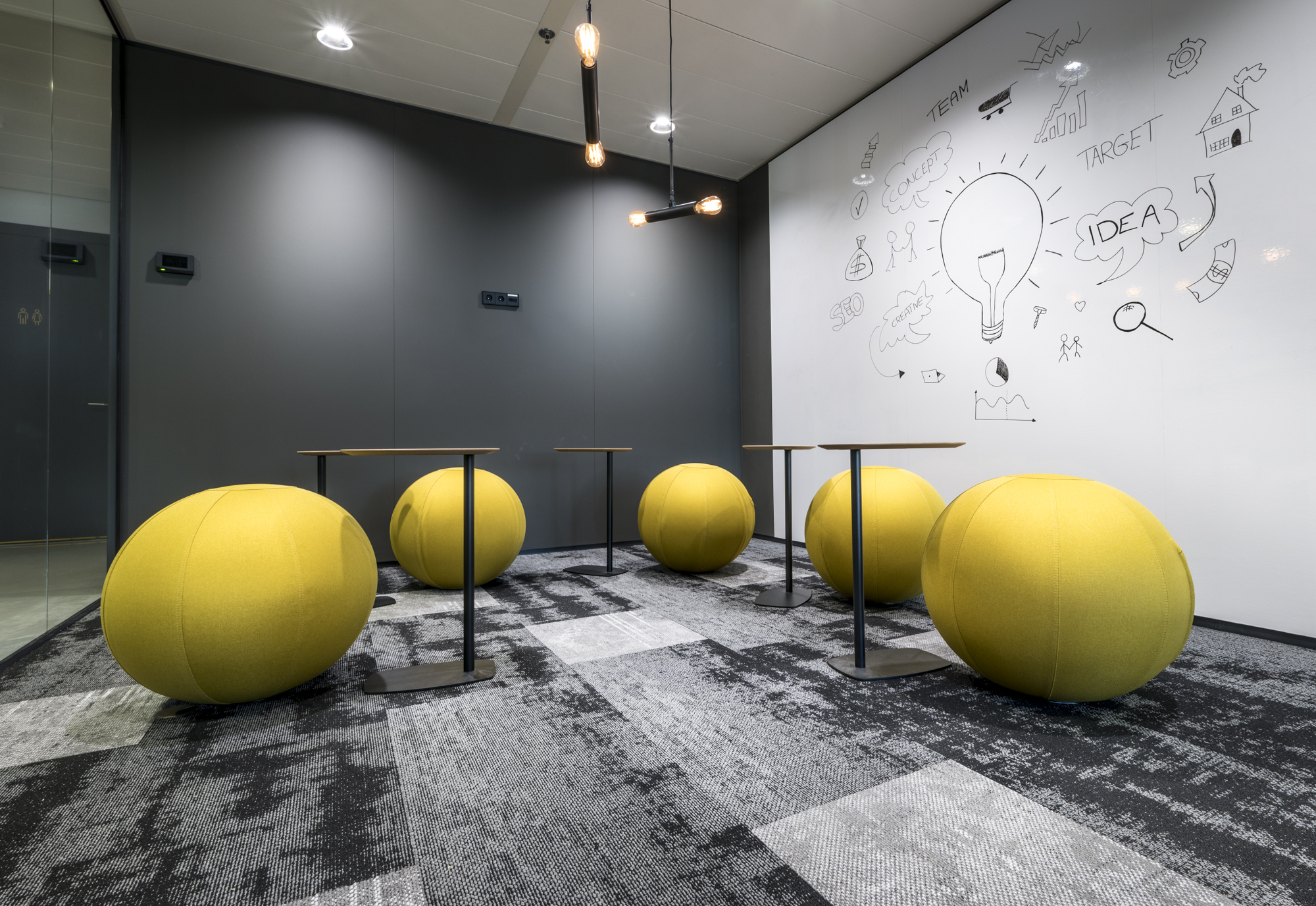 Een brainstormruimte met gele zitballen, tafels en een muur vol schetsen en ideeën.