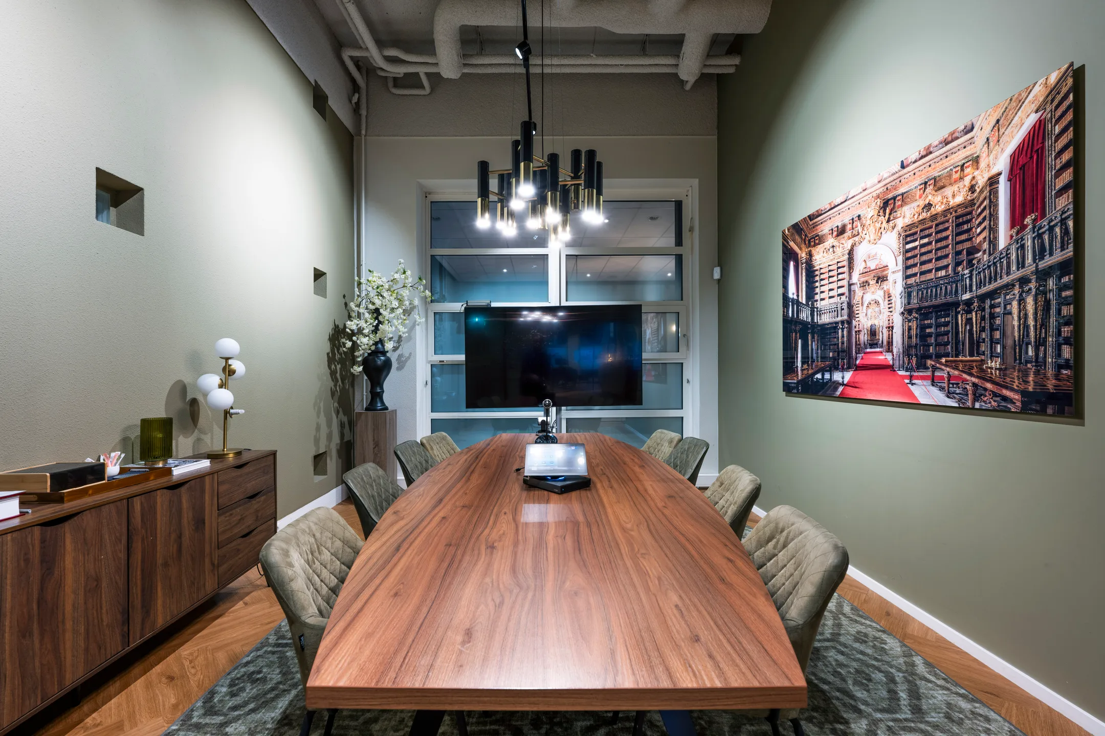 Vergaderruimte met een lange houten tafel, moderne verlichting, een groot scherm en een kunstwerk aan de muur.