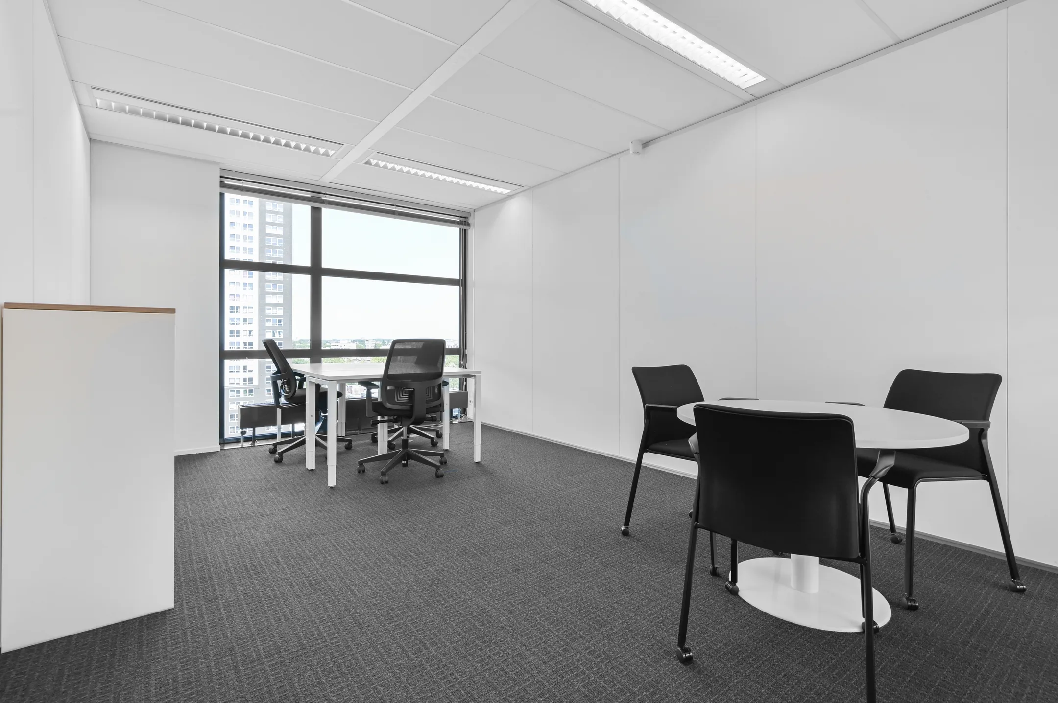 Een moderne kantoorruimte met bureaustoelen, een bureau en een ronde tafel met stoelen.