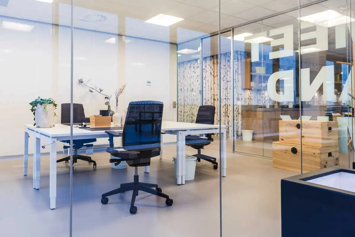 Modern glazen kantoor met bureaus, bureaustoelen en planten bij Bisonspoor.