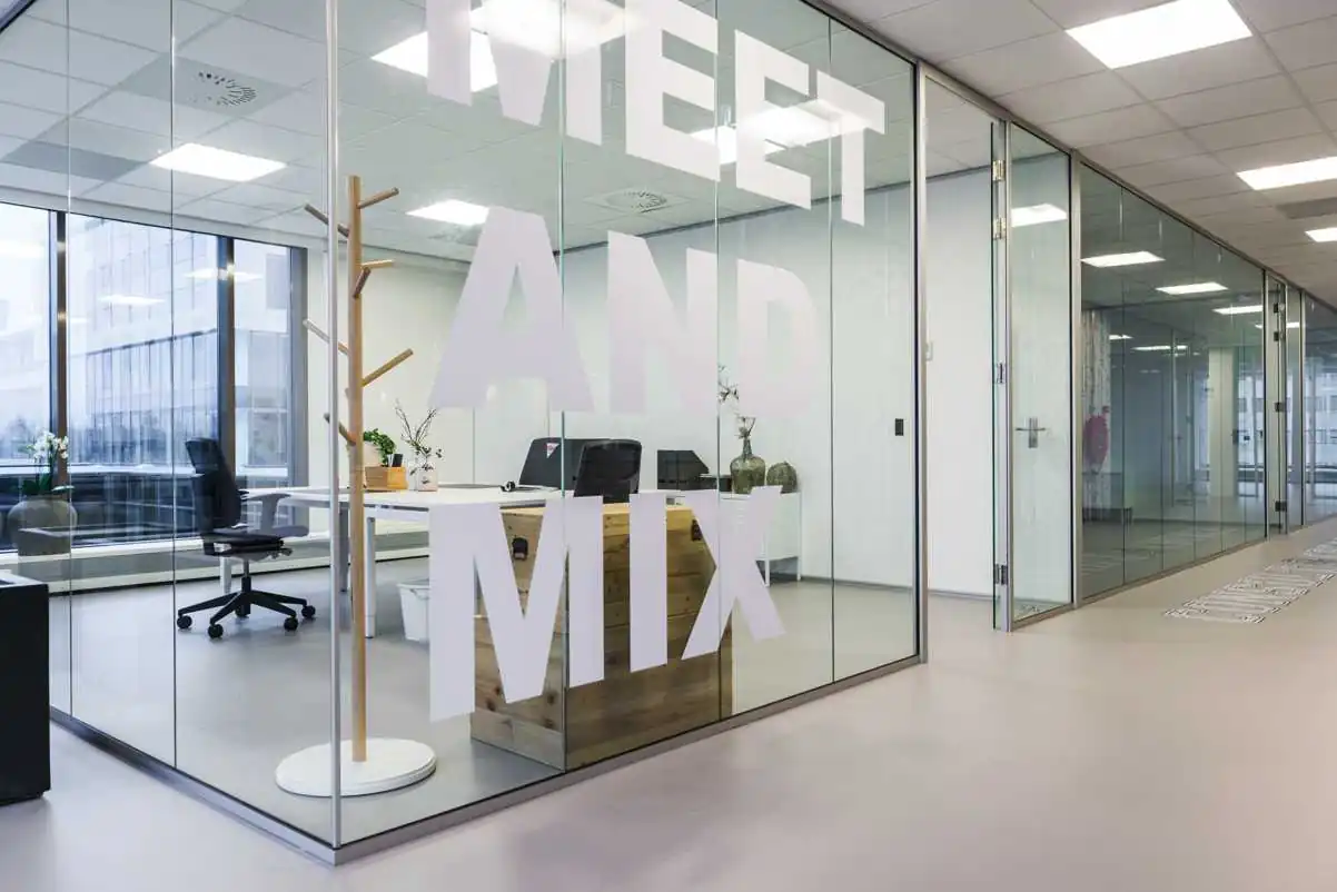 Moderne kantoorruimte met glazen wanden en de tekst "MEET AND MIX" groot op het glas.