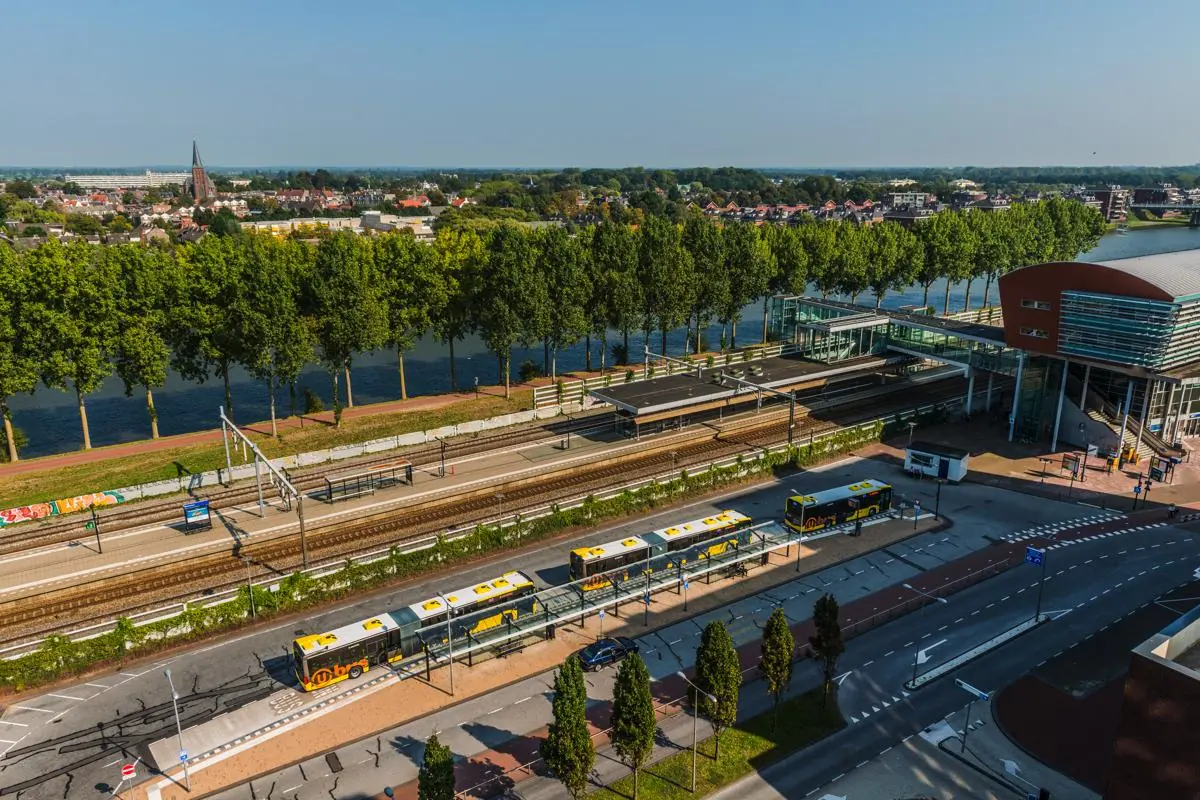 Luchtfoto van station Bisonspoor in Maarssen met treinsporen, bussen en een moderne stationshal langs het water.